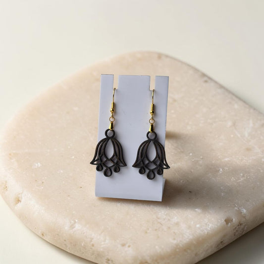 Bluebell Flower Earrings by Mirabilia Boutique, crafted from lasercut walnut wood with a delicate floral design, displayed on a white stand atop a smooth beige stone surface.