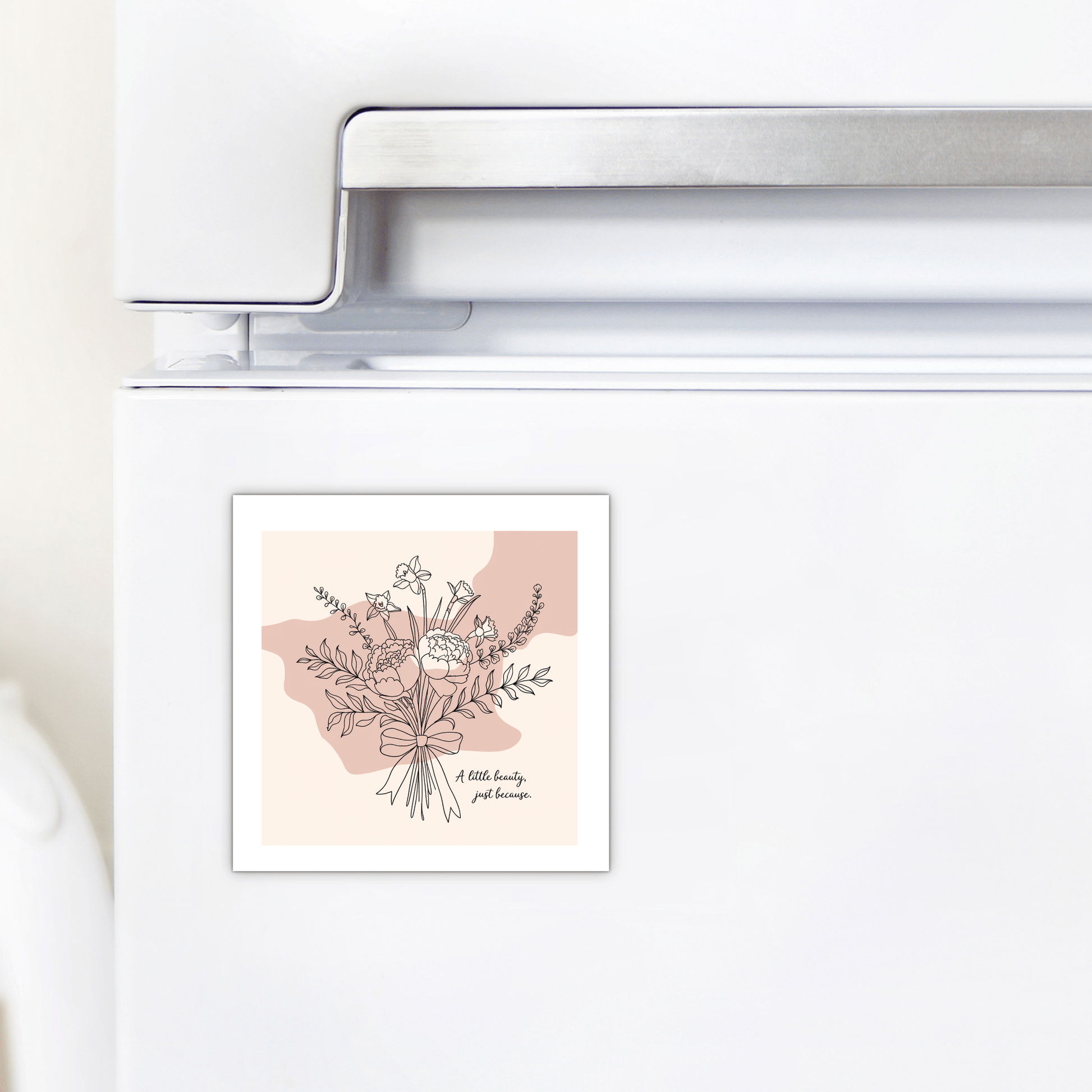 A white fridge with Mirabilia Boutique’s “A Little Beauty Magnet – Just Because Floral Gift,” featuring a flower bouquet line drawing on beige and pink with the phrase “A little beauty goes a long way.” Ideal as a thinking of you gift.