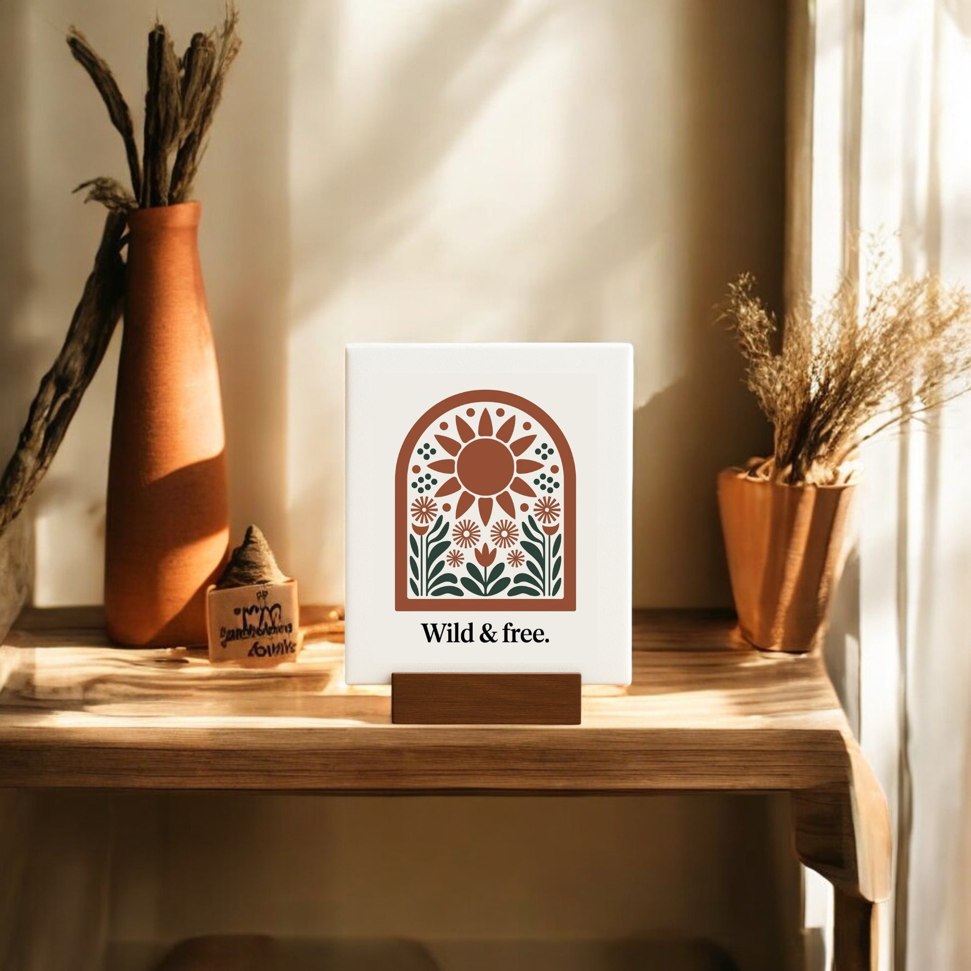 The Wild & Free Mini Sign – Sunflower Boho Desk Art by Mirabilia Boutique sits on a wooden table, surrounded by dried plants and warm sunlight, creating a cozy, boho-inspired look for nature decor lovers.