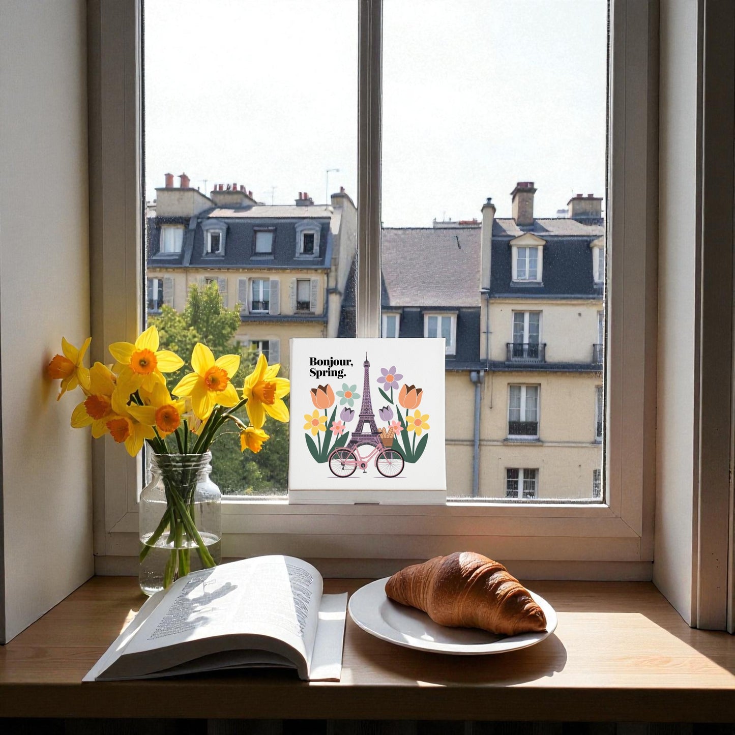 Create a cozy Parisian vibe with the "Bonjour, Spring Canvas – Eiffel Tower Floral Art" by Mirabilia Boutique, featuring yellow daffodils, an open book, croissant, and Paris buildings for a charming spring scene.