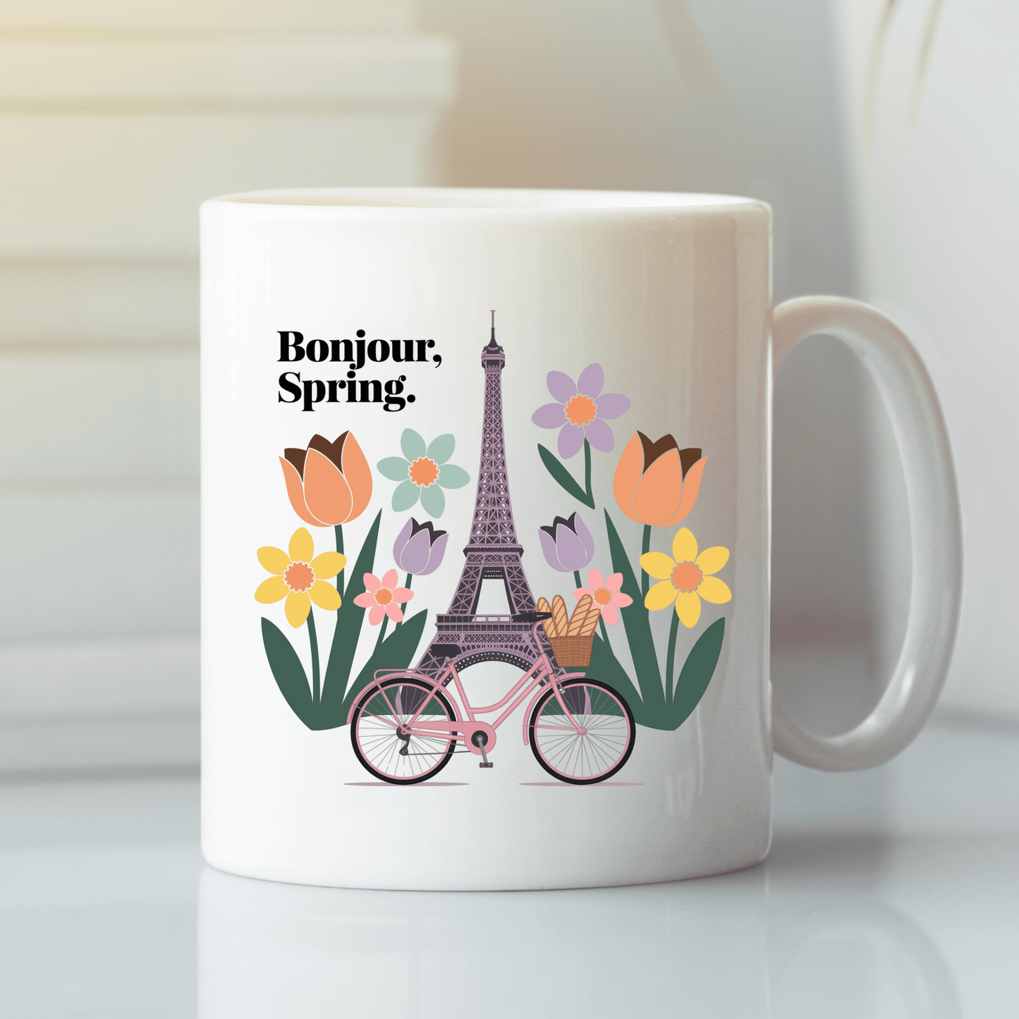 The Bonjour Spring Paris Mug – Eiffel Tower & Florals by Mirabilia Boutique features a white ceramic design with an Eiffel Tower, colorful flowers, a pink bicycle with baguettes, and "Bonjour, Spring." for a charming Parisian vibe.