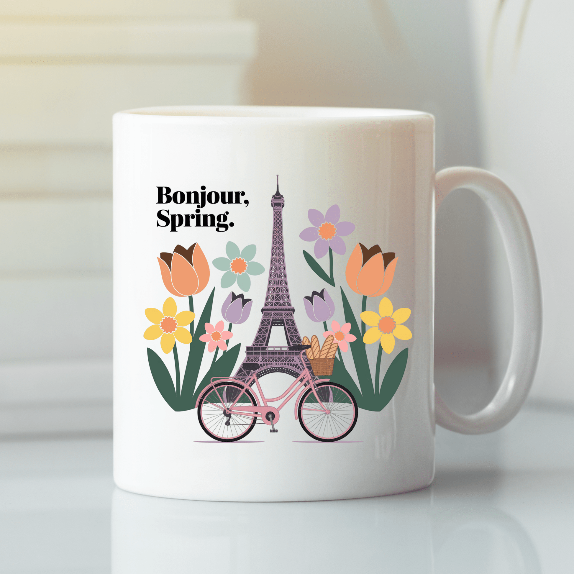 The Bonjour Spring Paris Mug – Eiffel Tower & Florals by Mirabilia Boutique features a white ceramic design with an Eiffel Tower, colorful flowers, a pink bicycle with baguettes, and "Bonjour, Spring." for a charming Parisian vibe.