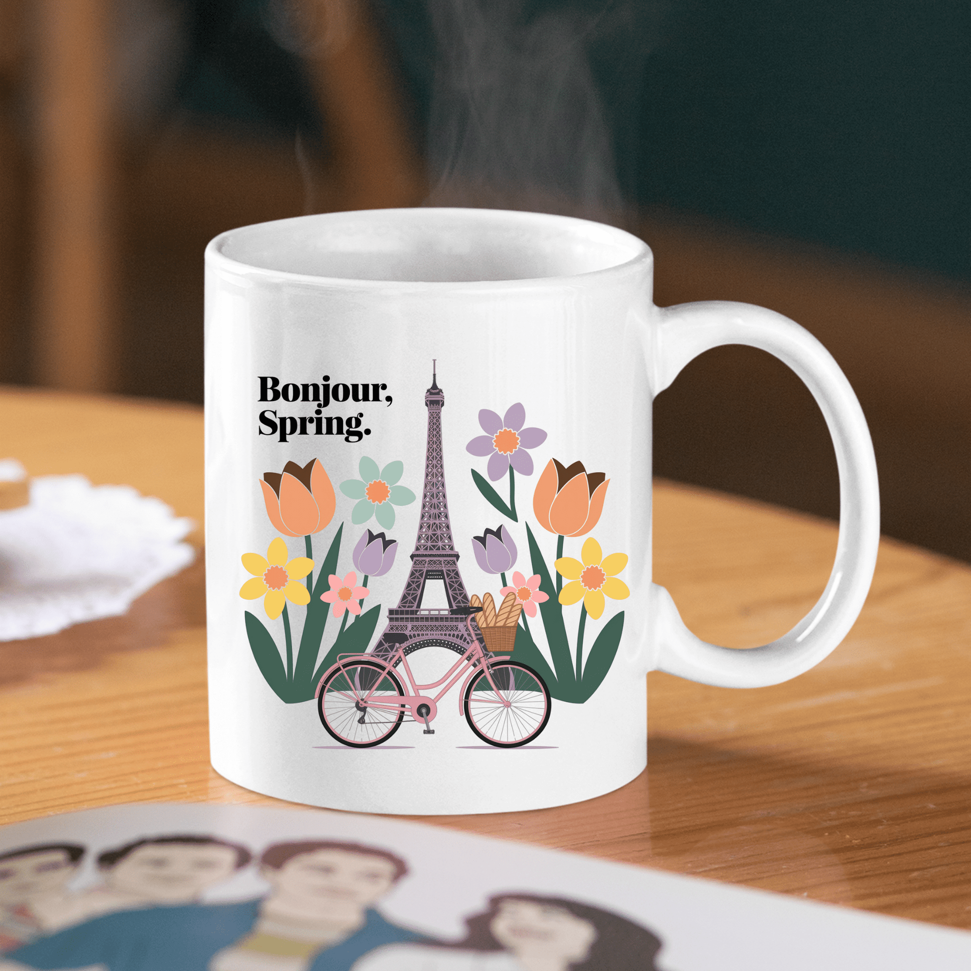 Sip your Parisian coffee from the Mirabilia Boutique Bonjour Spring Paris Mug – Eiffel Tower & Florals, featuring “Bonjour, Spring.” with vibrant blooms and a pink bicycle—perfect for brightening your mornings.