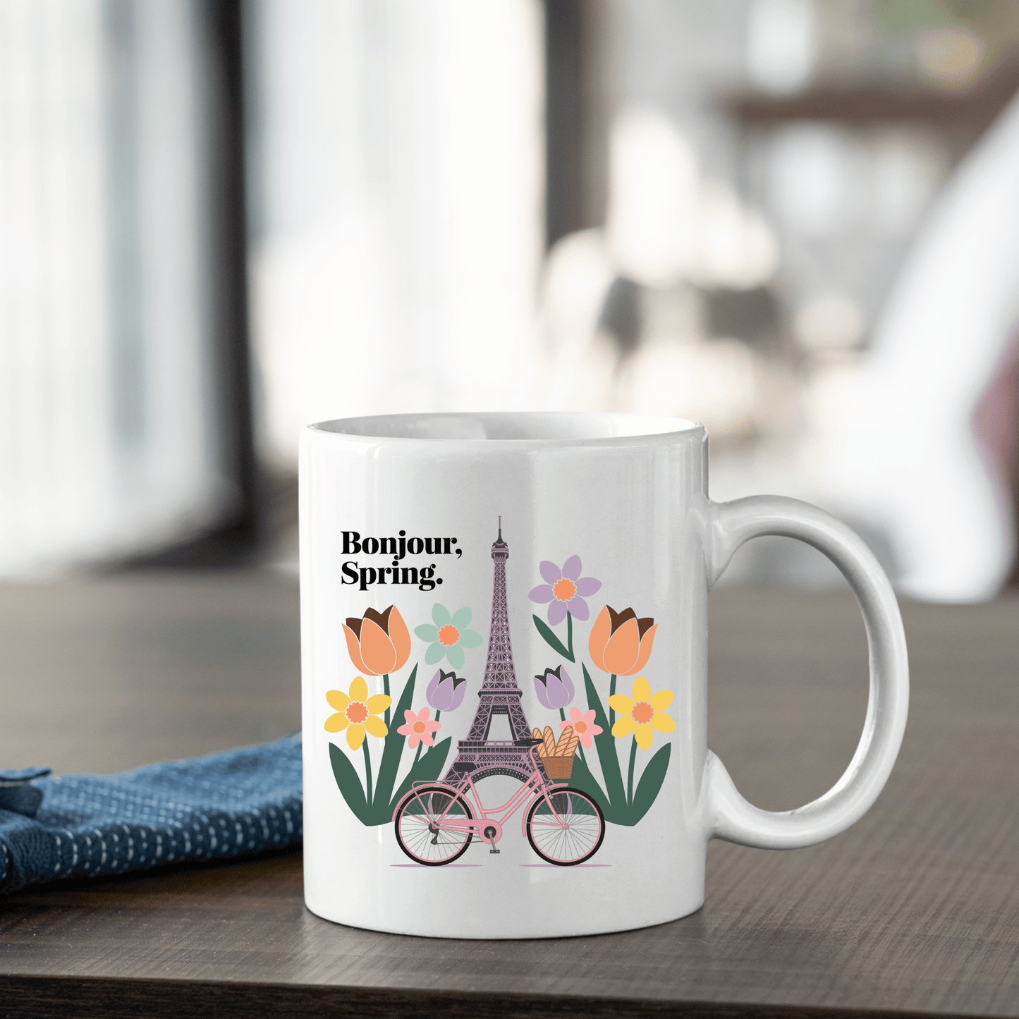 The Mirabilia Boutique "Bonjour Spring Paris Mug – Eiffel Tower & Florals" features an illustration of the Eiffel Tower, colorful flowers, and a pink bicycle with "Bonjour, Spring." in black text.
