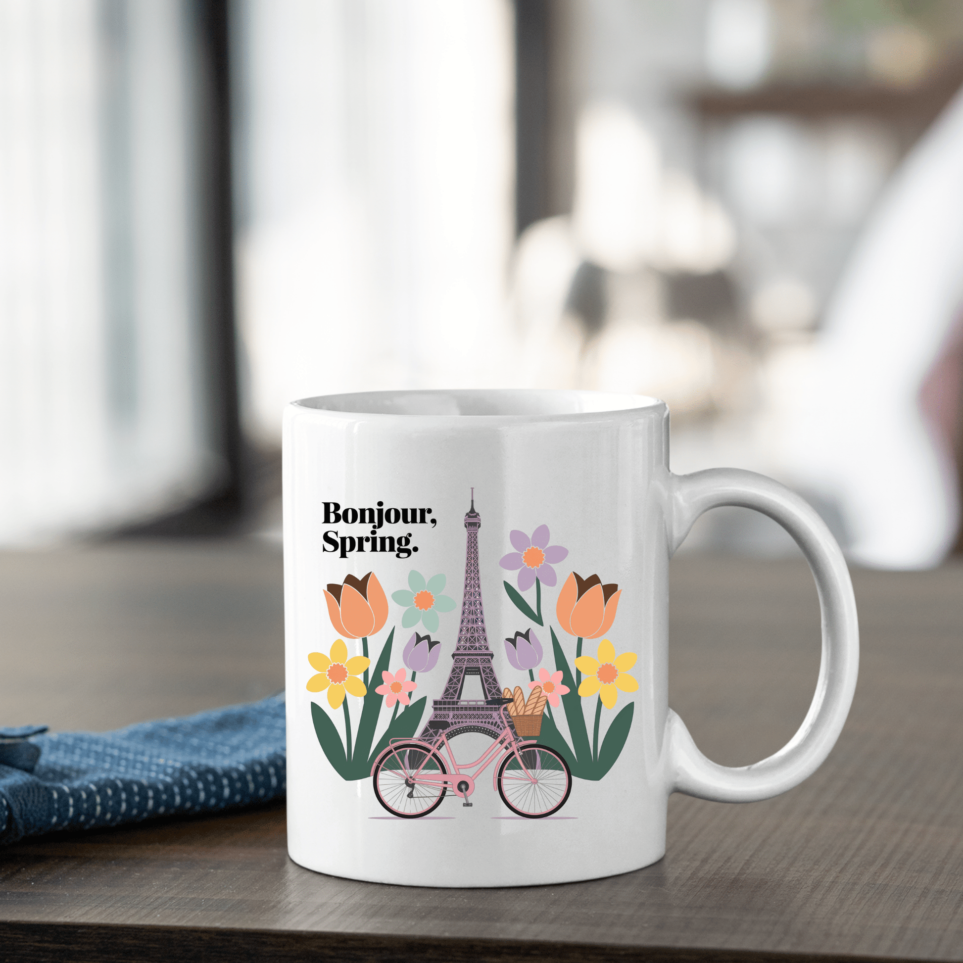 The Mirabilia Boutique "Bonjour Spring Paris Mug – Eiffel Tower & Florals" features an illustration of the Eiffel Tower, colorful flowers, and a pink bicycle with "Bonjour, Spring." in black text.