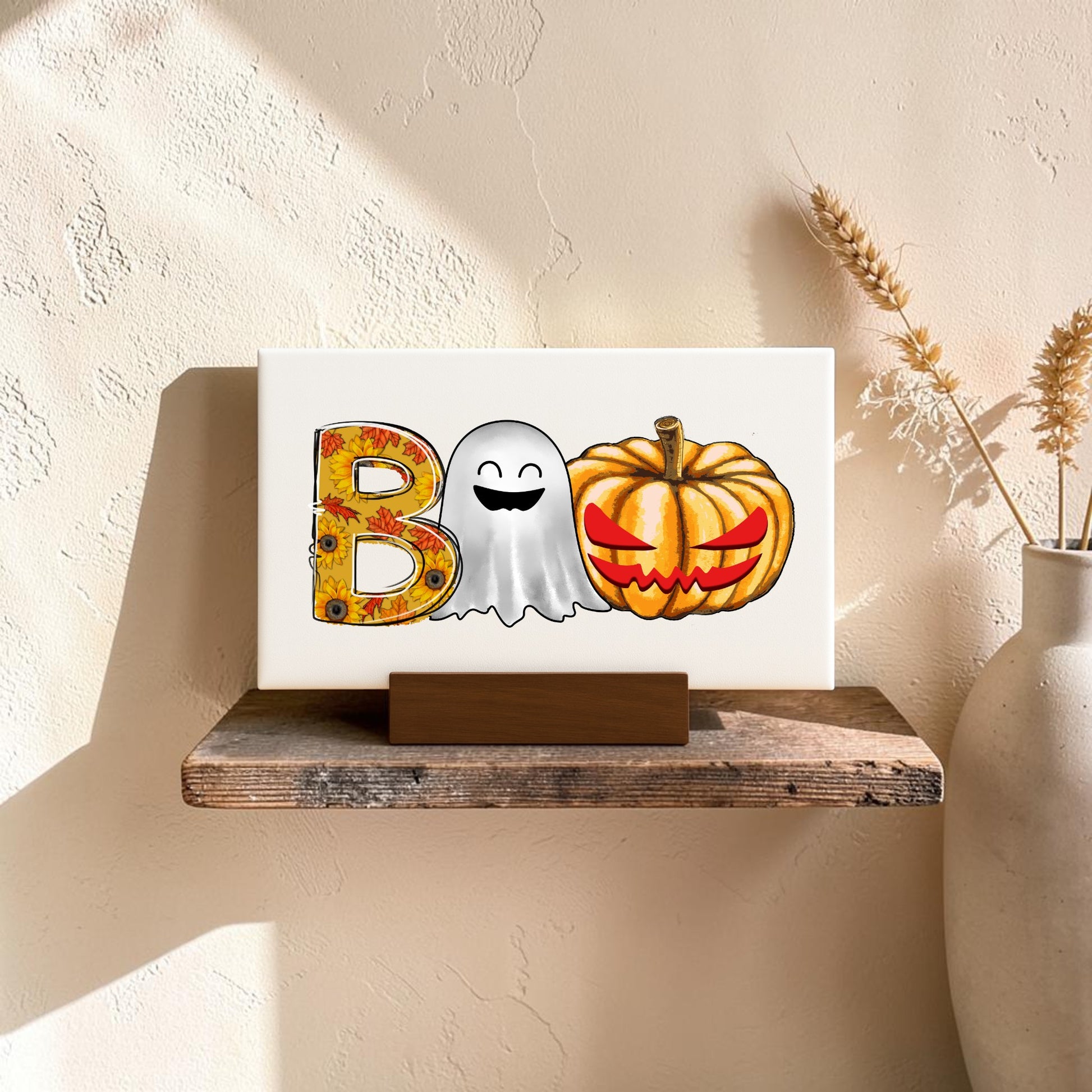 The BOO Ghost Pumpkin Mini Sign by Mirabilia Boutique adds festive Halloween charm to your shelf, while a beige vase with dried wheat beside it brings cozy autumn vibes against a textured cream wall.