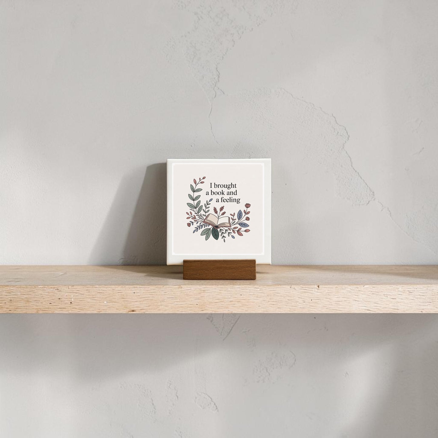 The "I Brought a Book and a Feeling Mini Sign" by Mirabilia Boutique features floral art and bookish text on a decorative tile with wooden stand—perfect literary decor for shelves or as a charming gift for book lovers.