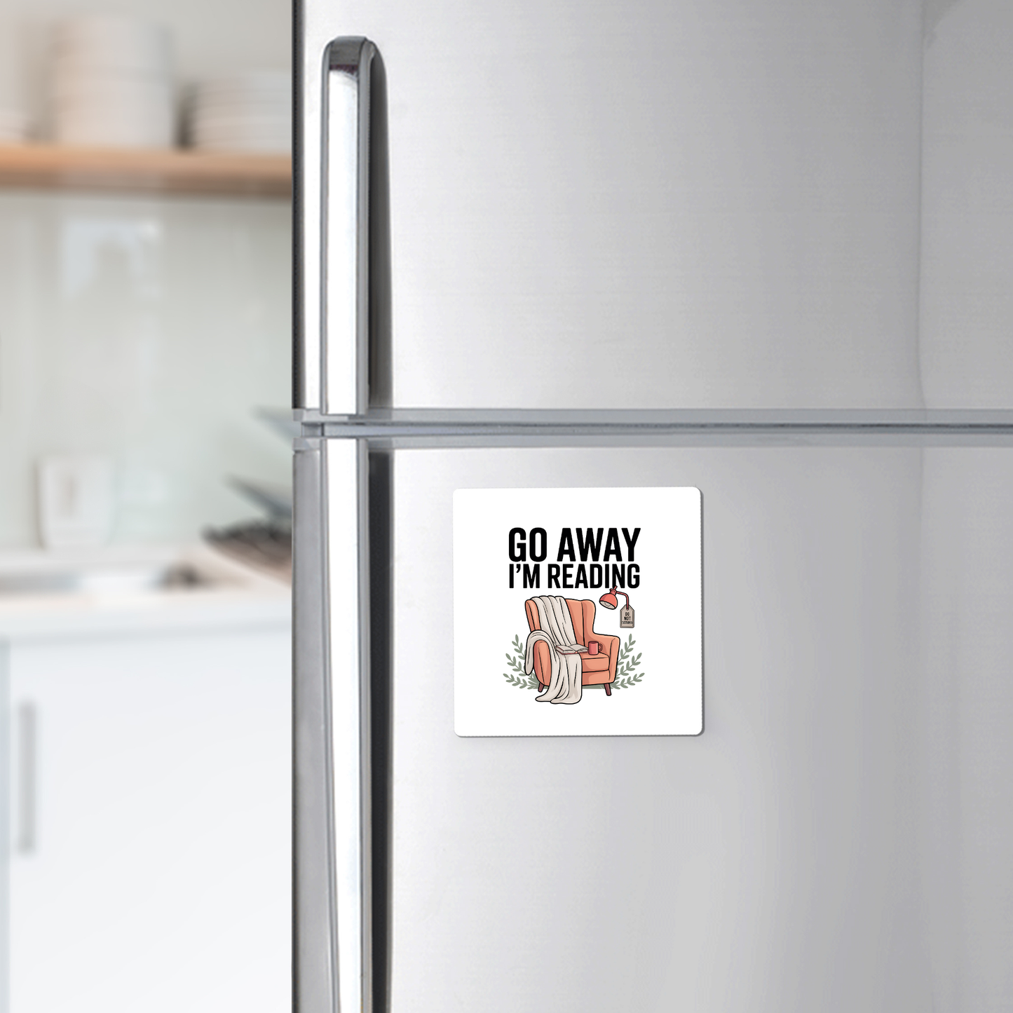 The Go Away I'm Reading Magnet by Mirabilia Boutique features "GO AWAY I'M READING" above a cozy armchair, book, and coffee. This funny book lover gift makes perfect decor for any reader’s fridge.