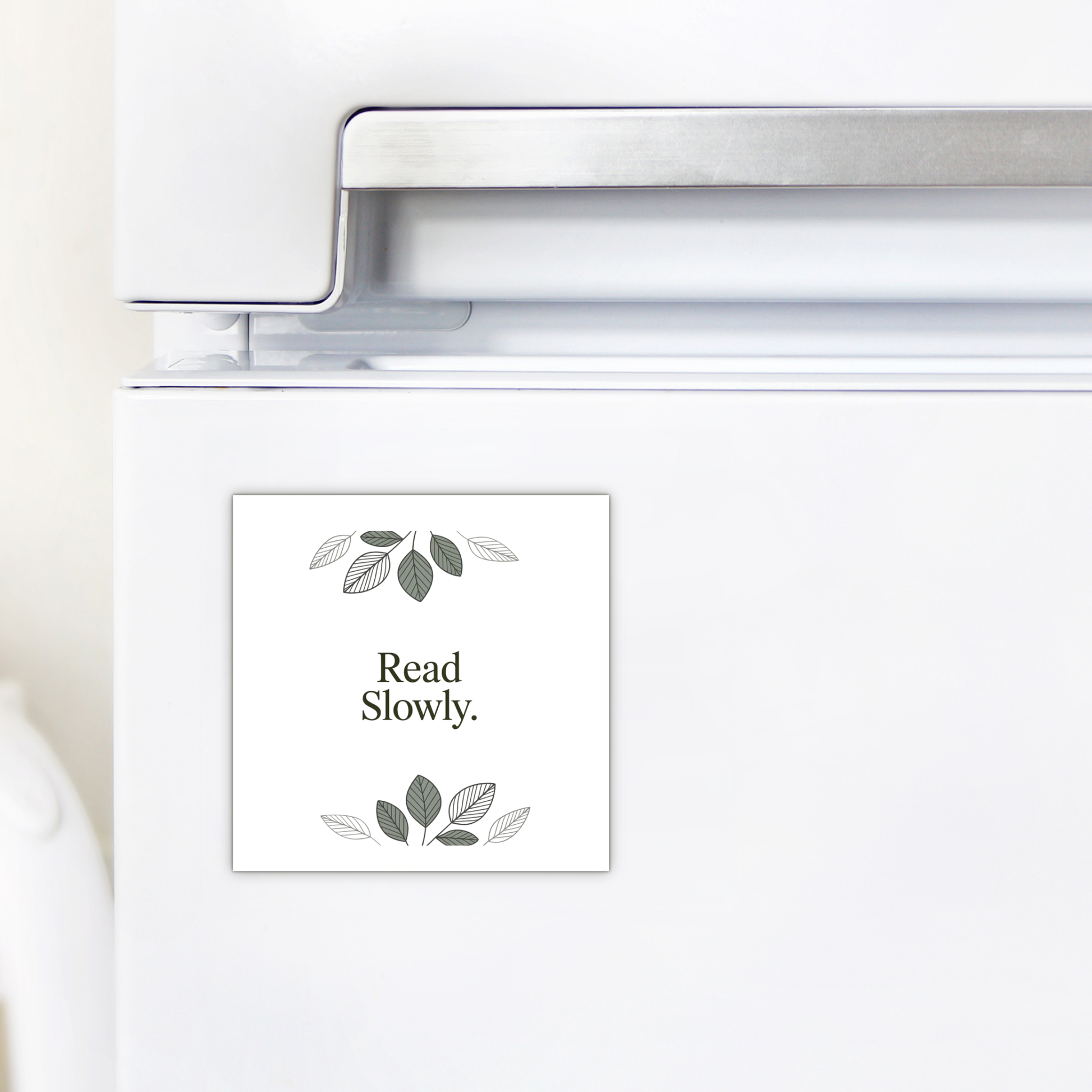 The Read Slowly Book Lover Magnet by Mirabilia Boutique features simple green and gray leaf illustrations—a charming literary decor piece and thoughtful gift for any book lover.