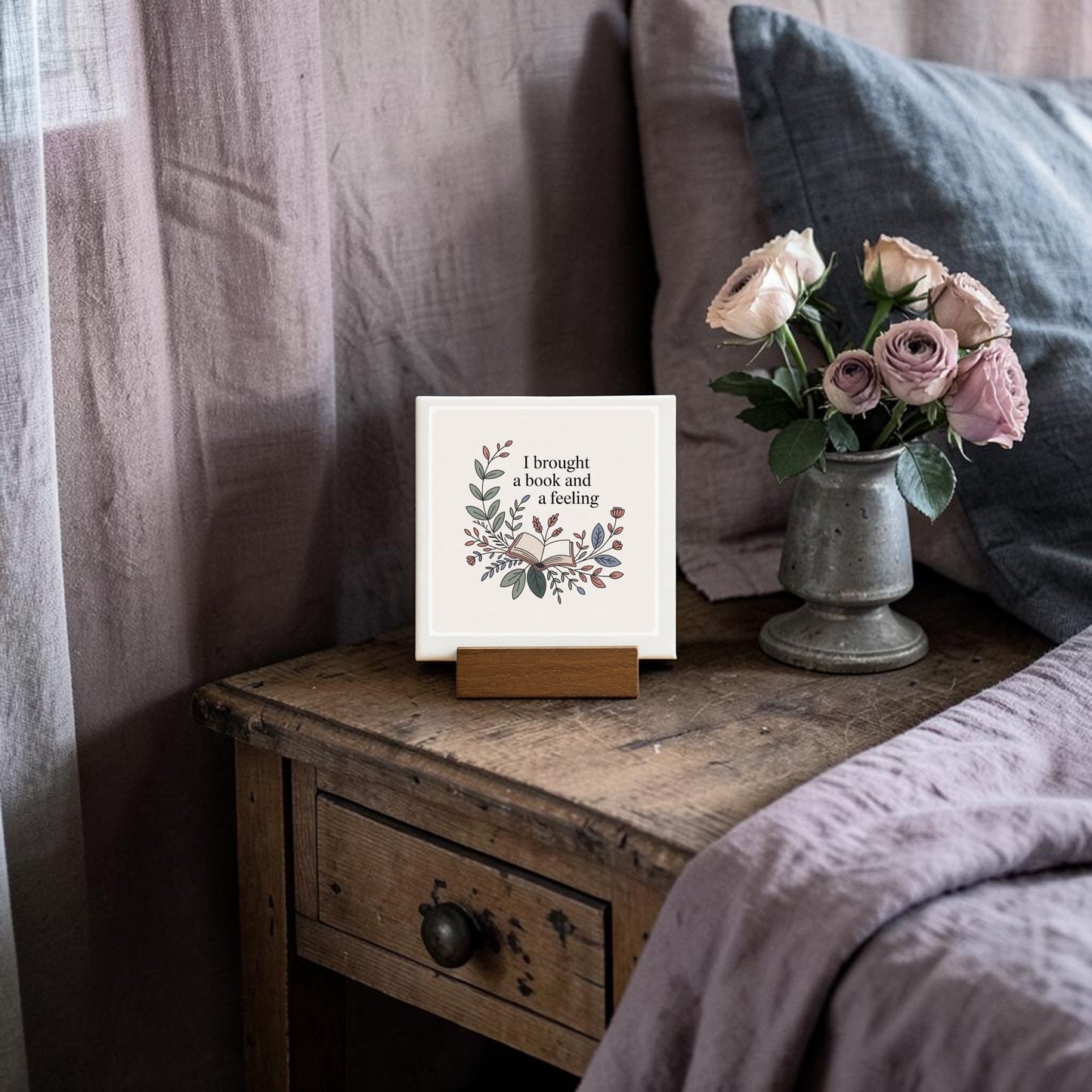 The Mirabilia Boutique “I Brought a Book and a Feeling” Mini Sign adds literary charm to your decor, displayed on a wooden nightstand with roses and muted bedding. It’s the perfect gift for book lovers.