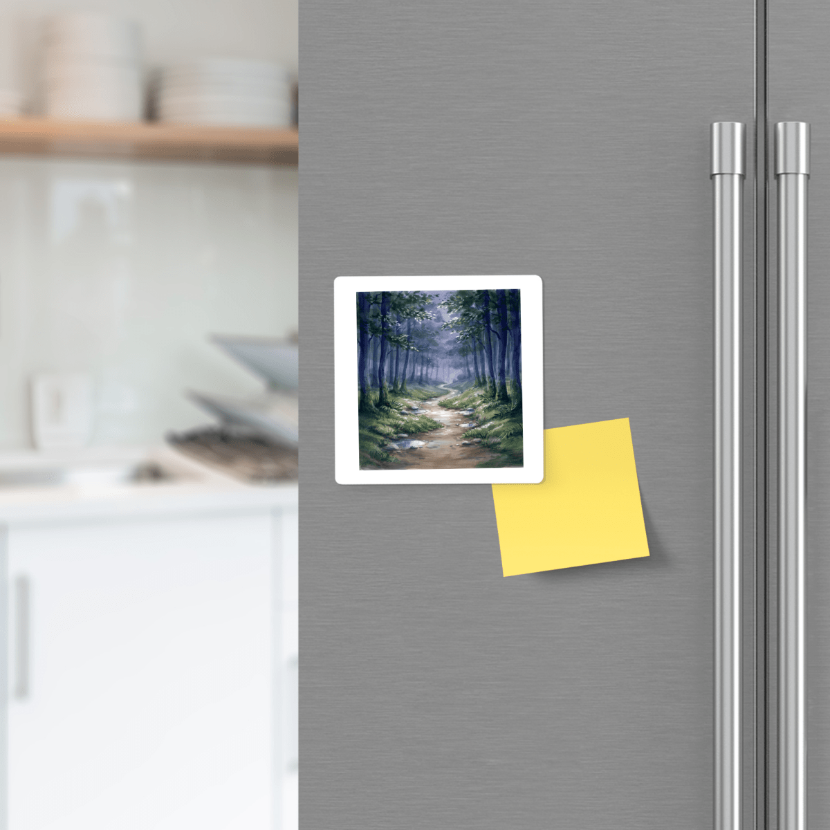 A refrigerator door features the Mirabilia Boutique Borrow a Little Moonlight Forest Magnet, displaying a small forest path photo, alongside a blank yellow sticky note. Blurred kitchen shelves and dishes are visible in the background.