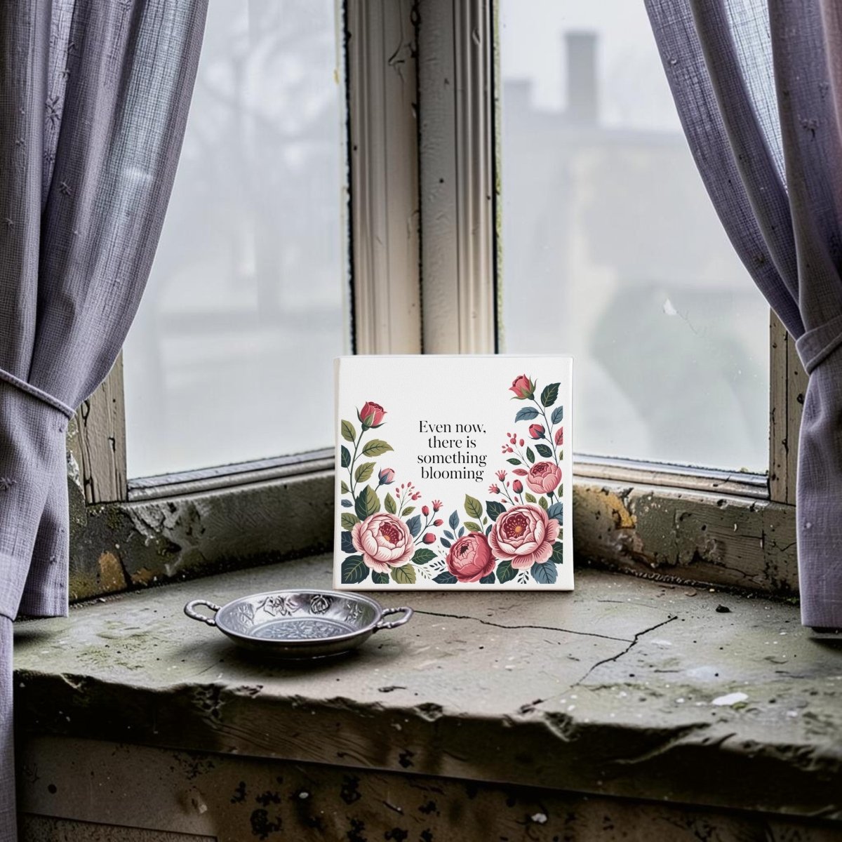 The "Even Now There Is Something Blooming" canvas wall art by Mirabilia Boutique rests on a weathered windowsill with a decorative dish—an encouragement gift framed by sheer purple curtains and a foggy view, like living hope.