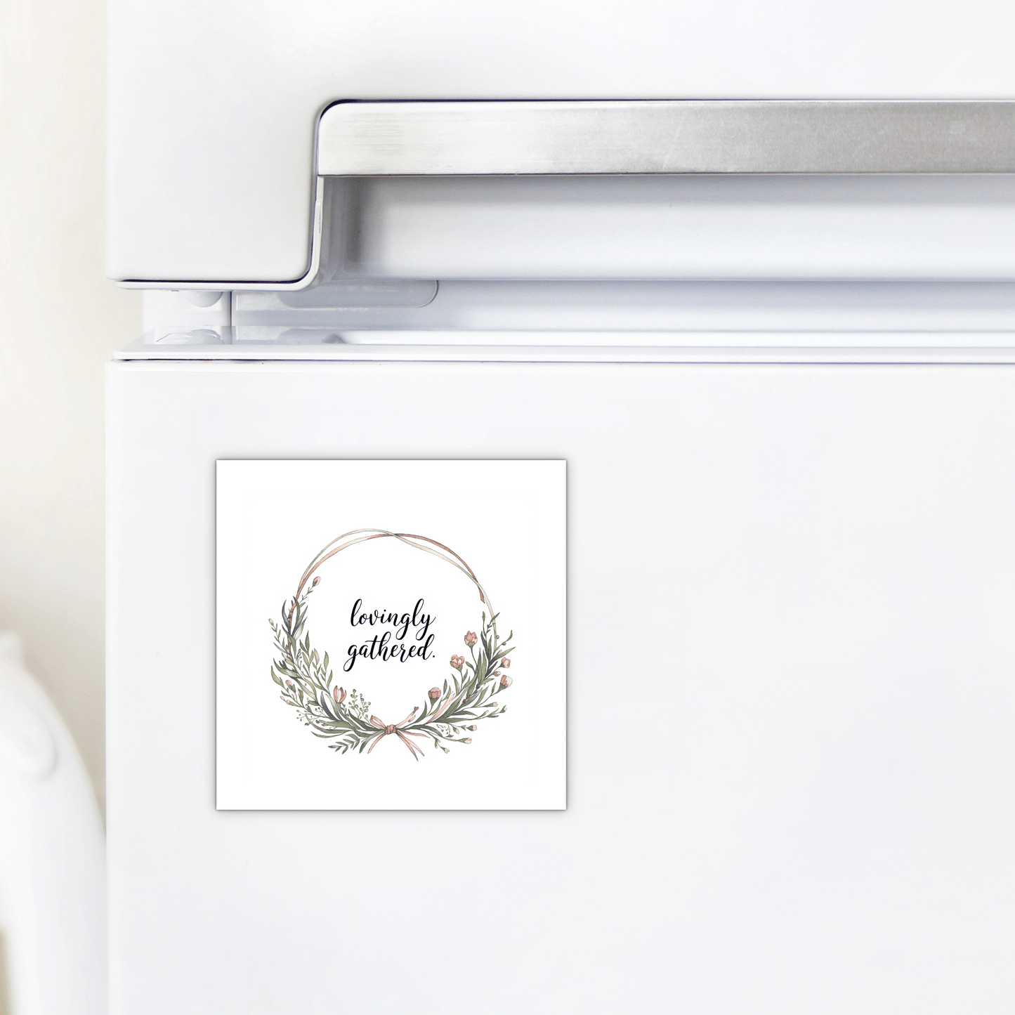 A white fridge displays the Mirabilia Boutique "Lovingly Gathered Magnet," featuring a watercolor floral wreath and elegant script, ideal for farmhouse decor.