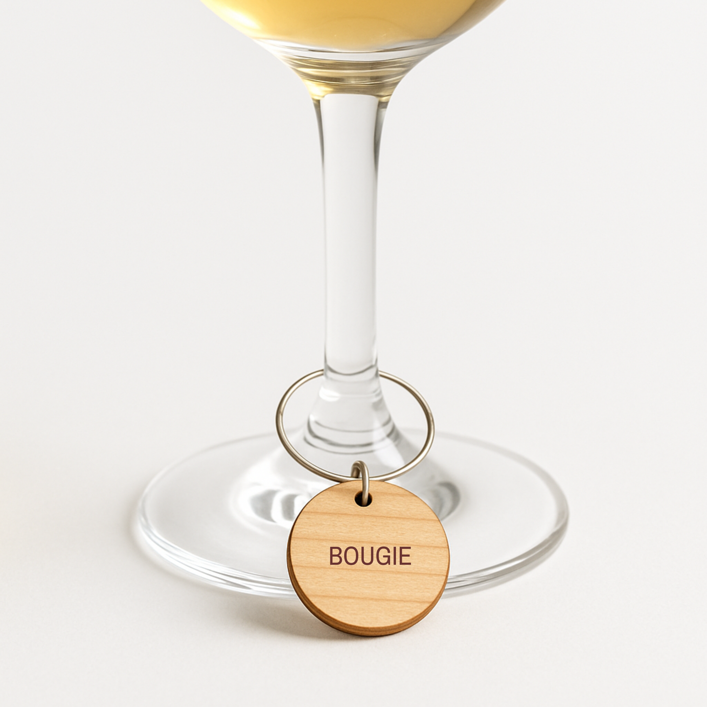 A “BOUGIE” engraved wooden wine glass charm from the Mirabilia Boutique Bridal Party Personality Wine Charms | Set of 8 adds a touch of personality to any wine glass filled with white wine, making it an elegant and perfect choice for bridal party gifts and bridal wine charm collections.