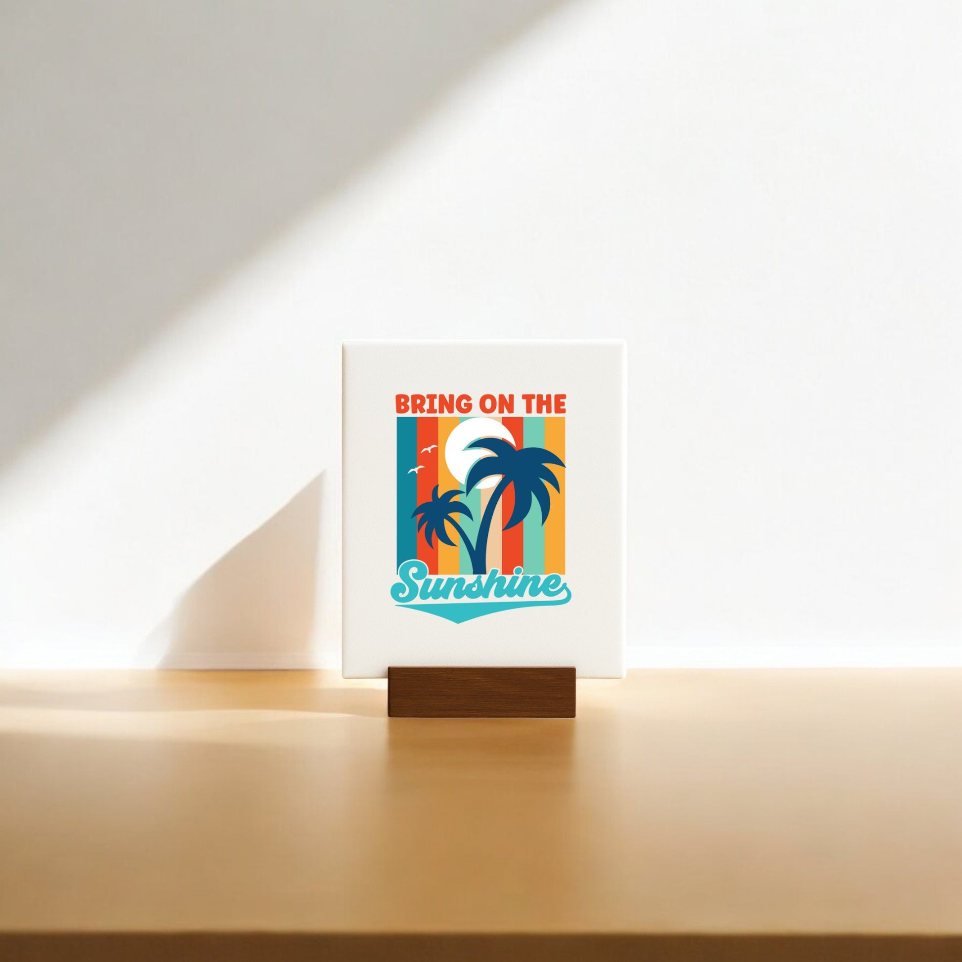 The Bring on the Sunshine Canvas – Retro Palm Tree Art by Mirabilia Boutique features a retro sunset with palm trees and uplifting text. This mini decor piece comes with a wooden stand, perfect for adding coastal charm to any sunlit space.