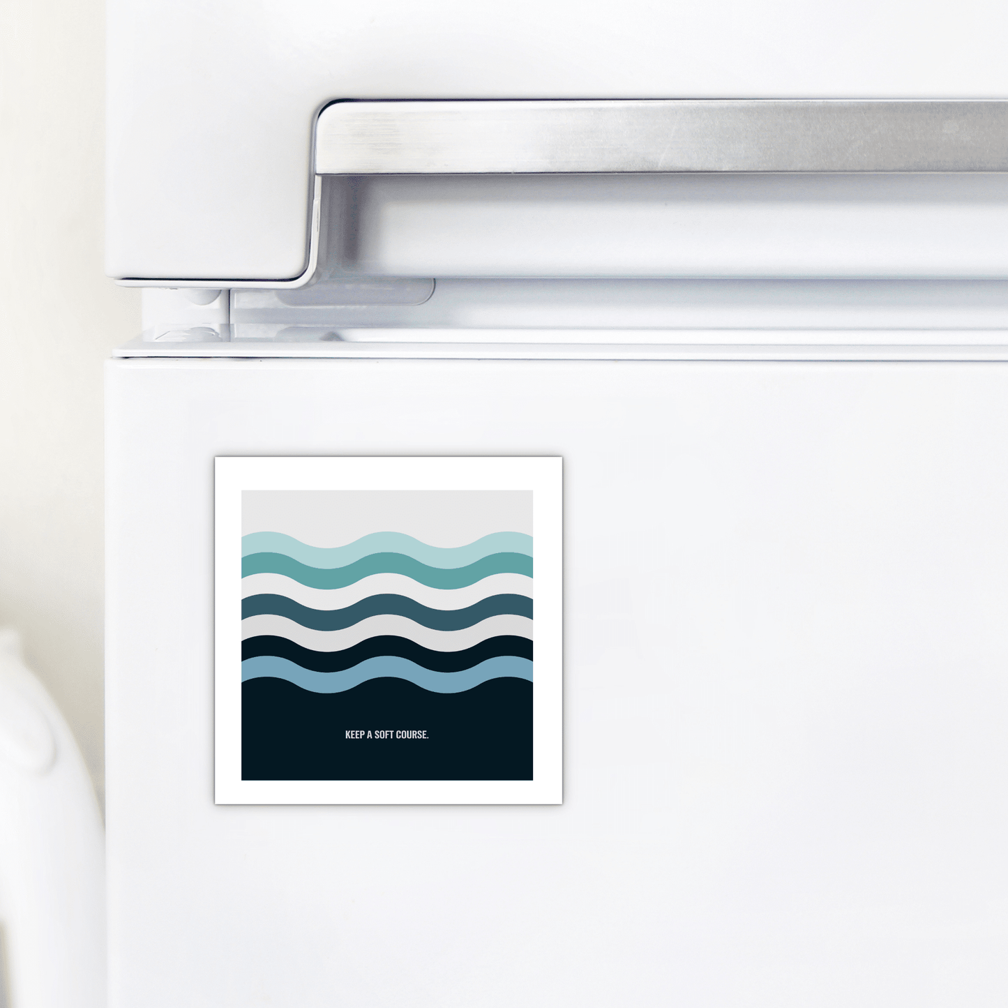 The Keep a Soft Course Magnet by Mirabilia Boutique, featuring minimalist ocean-inspired wavy blue lines and the phrase "KEEP A SOFT CURRENT," adds a stylish touch to any white refrigerator, perfect for modern decor.