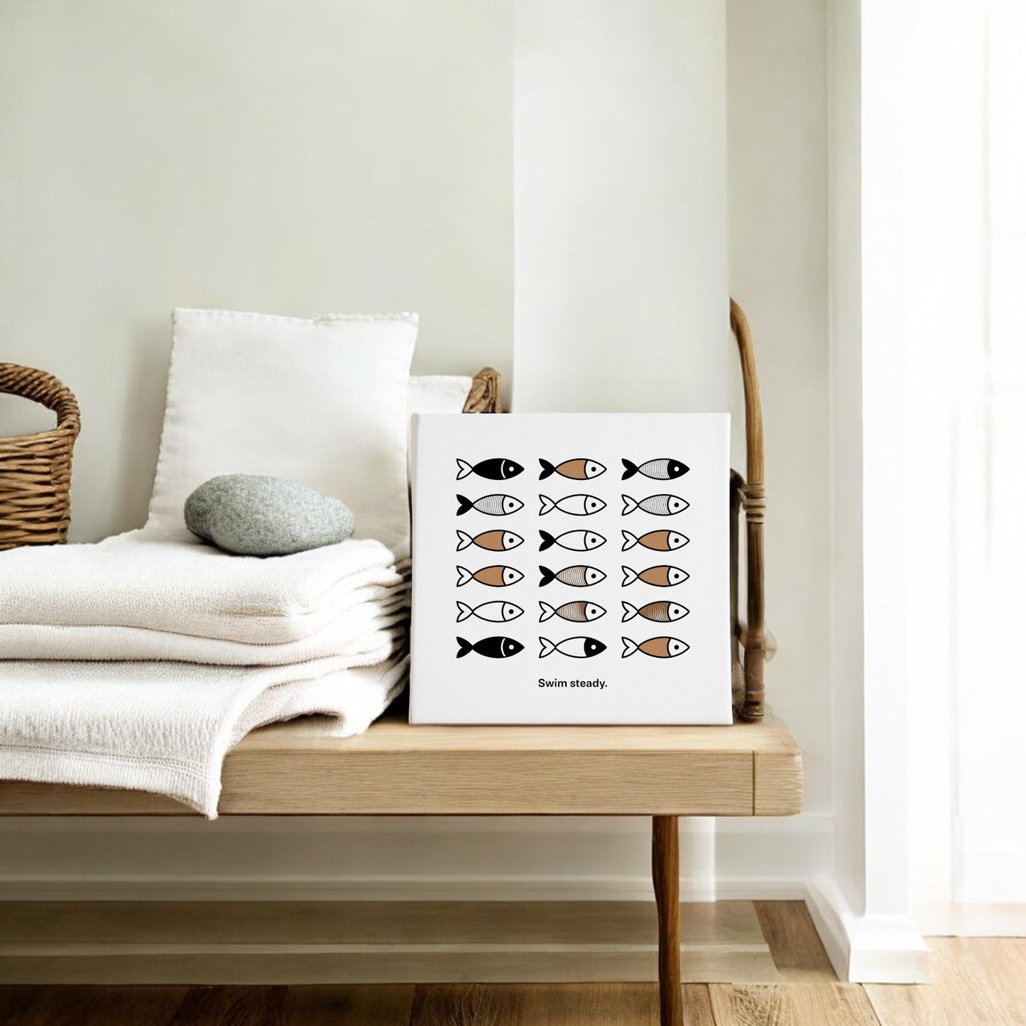 A minimalist room with a wooden bench, folded white towels, and a basket is elevated by Mirabilia Boutique’s "Swim Steady Canvas – Minimalist Neutral Wall Art, 8x8," featuring black and gold fish—an elegant encouragement gift for any space.