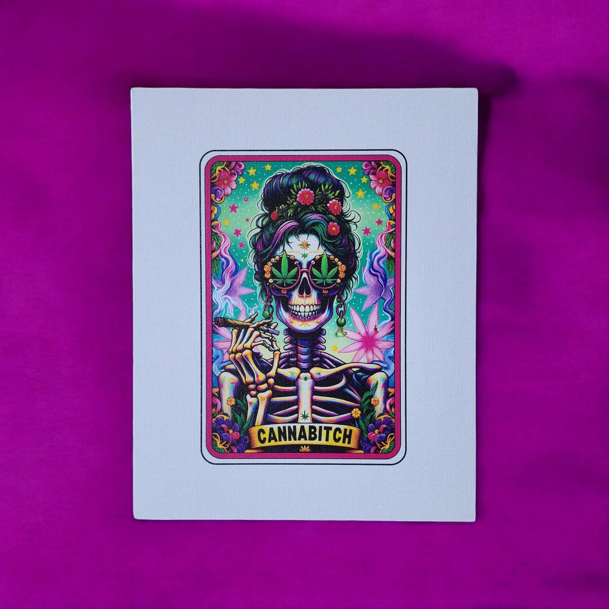 A vibrant painting on the Cannabitch 8x10 Canvas Sign by Mirabilia Boutique features a skeleton with an elaborate hairdo, adorned in large marijuana leaf-shaped sunglasses, and smoking a joint. The background bursts with dynamic patterns and stars, all set against a rich purple backdrop. The word "CANNABITCH" is boldly written at the bottom of this striking artwork.