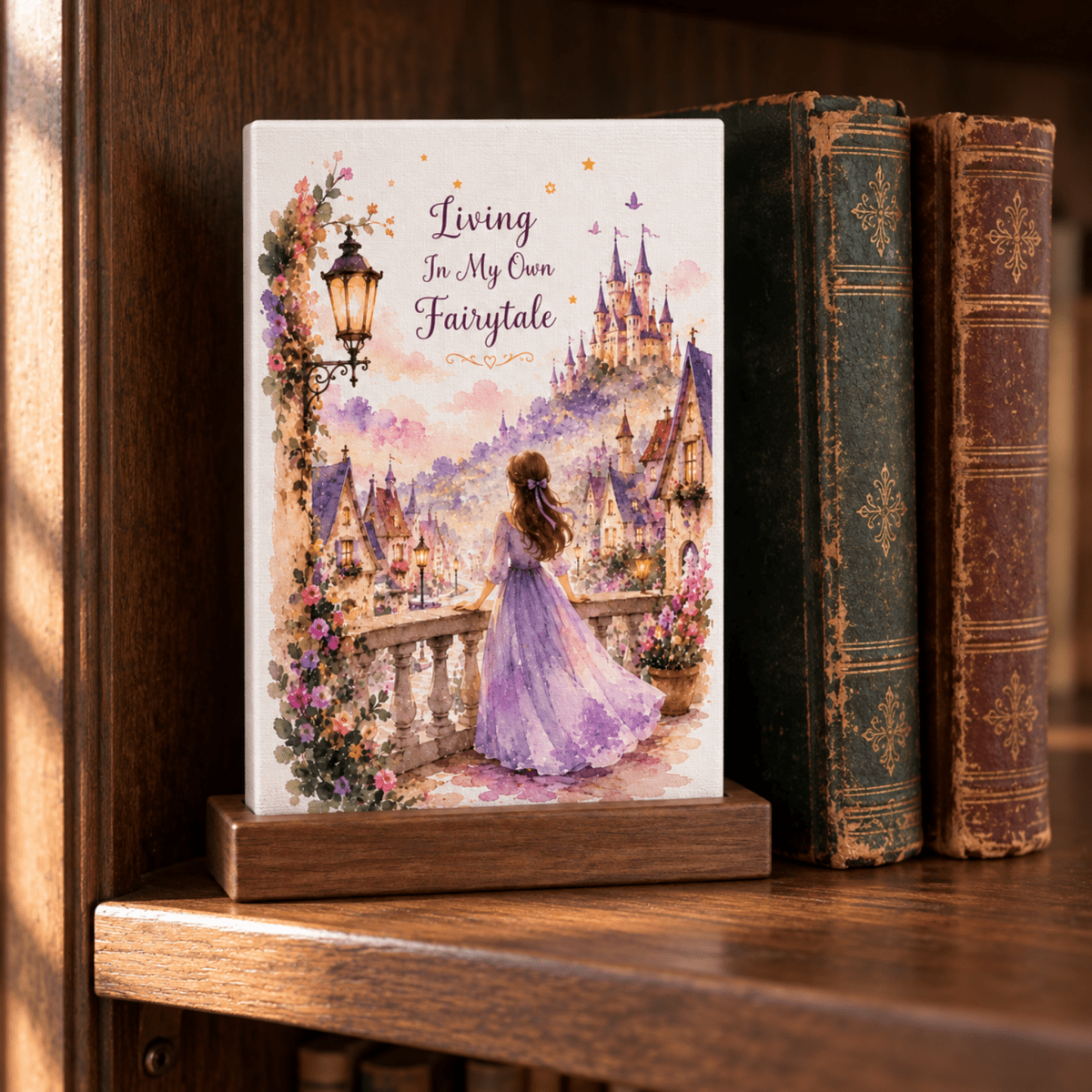 A Living in My Own Fairytale Mini Canvas on a wooden stand depicts a woman in a purple dress on a balcony overlooking a castle village, with the text “Living In My Own Fairytale” above her in a whimsical style.