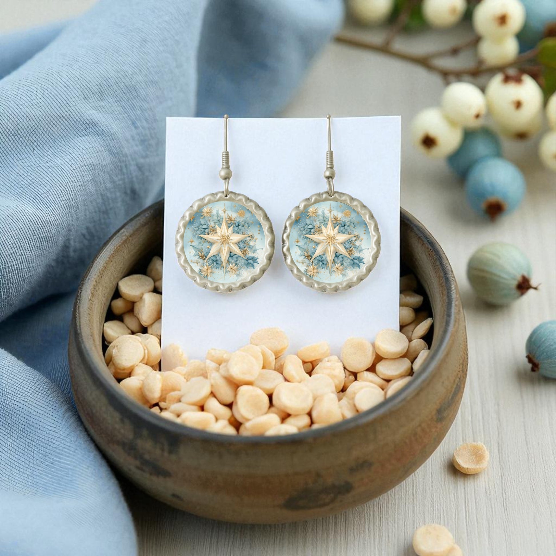 Celestial Star Earrings | Blue Floral Dangle Earrings by Mirabilia Boutique are shown on a display card in a ceramic bowl of beige lentils, accented with light blue cloth and decorative berries for a charming, botanical look.