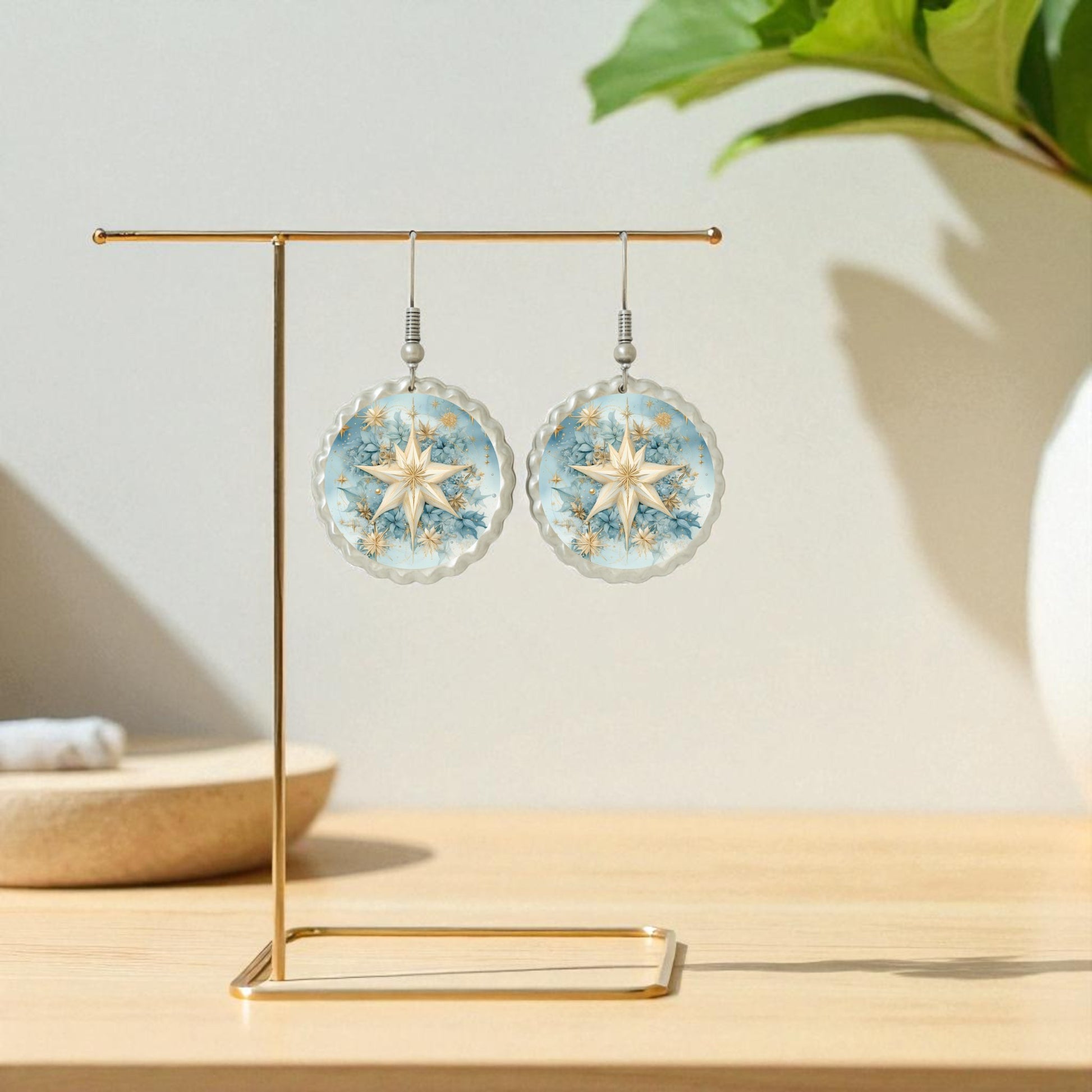 Celestial Star Earrings | Blue Floral Dangle Earrings by Mirabilia Boutique hang from a gold stand; a white plant pot and folded towel create a charming, softly lit backdrop.