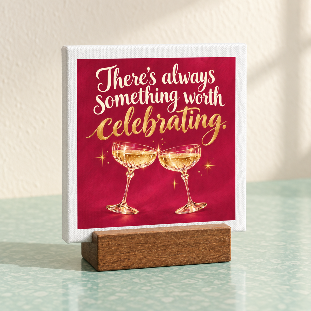 There’s Always Something Worth Celebrating Mini Bar Sign in a wooden stand, featuring the text “There’s always something worth celebrating” above an illustration of two clinking champagne coupes on a square mini canvas.