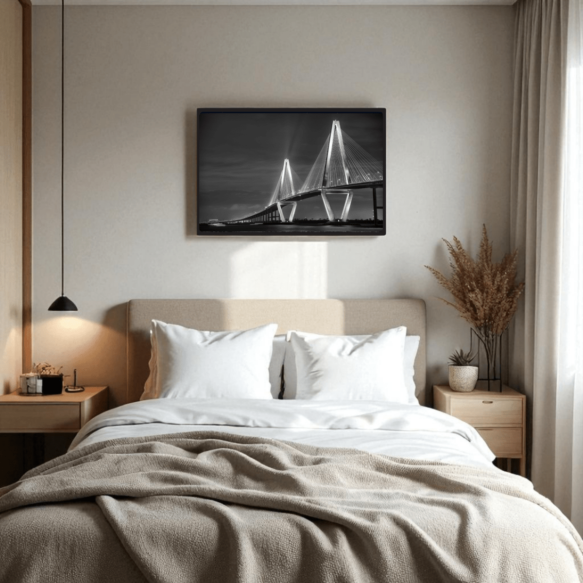 A cozy, modern bedroom features a beige bed, white pillows, wooden side tables, and Mirabilia Boutique's Ravenel Bridge Black & White Fine Art Print | Framed Art Print above the bed. Dried plants accent a side table by the window.