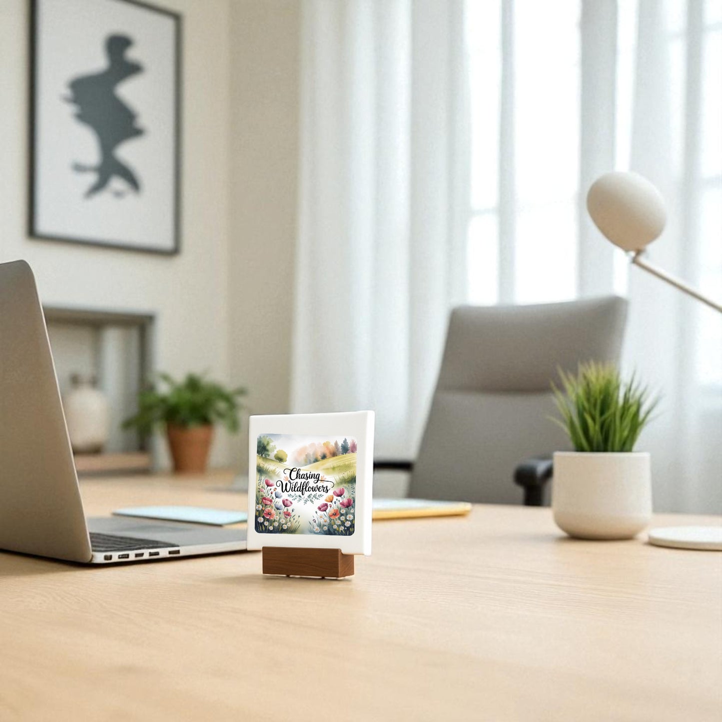 A Mirabilia Boutique “Chasing Wildflowers Mini Sign” sits beside a laptop and green plant on a modern office desk—perfect floral decor or meadowcore gift. Blurred chair and framed art complete this serene workspace scene.