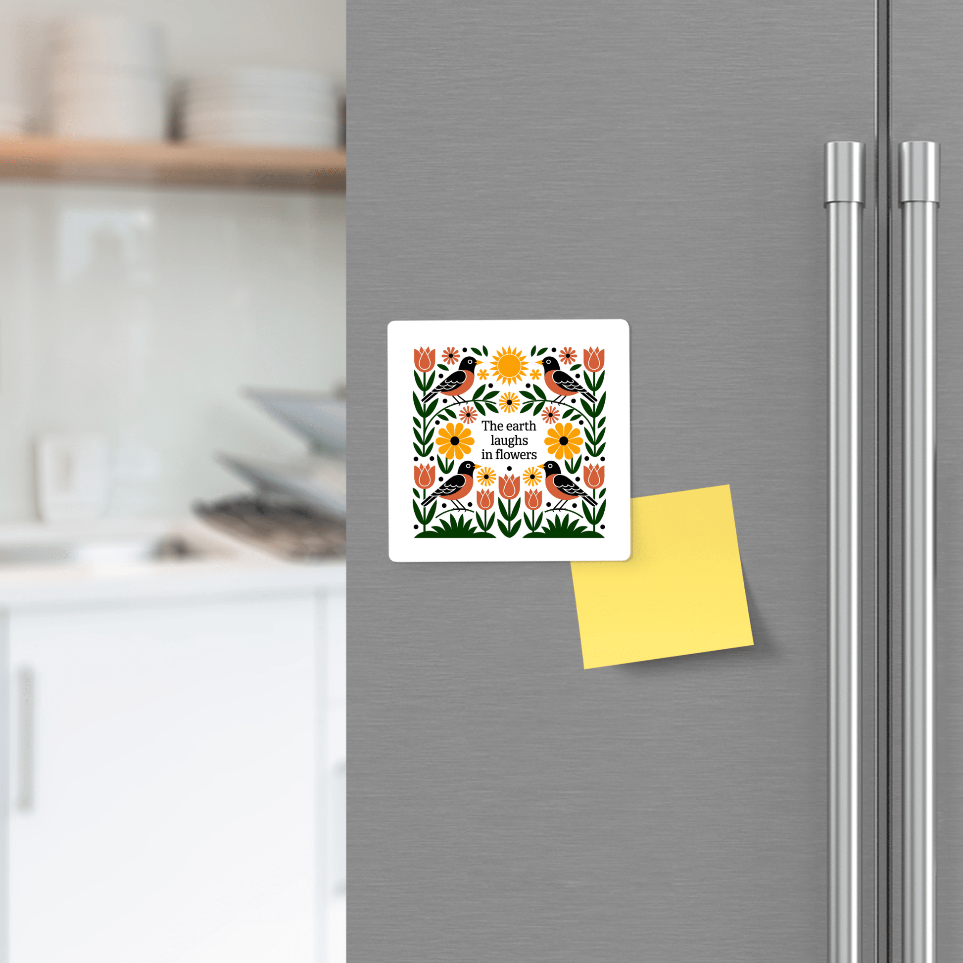 A kitchen scene shows a refrigerator door decorated with Mirabilia Boutique's The Earth Laughs in Flowers Floral Magnet above a yellow sticky note, blending garden-inspired decor with visible dishes on the counter in the background.