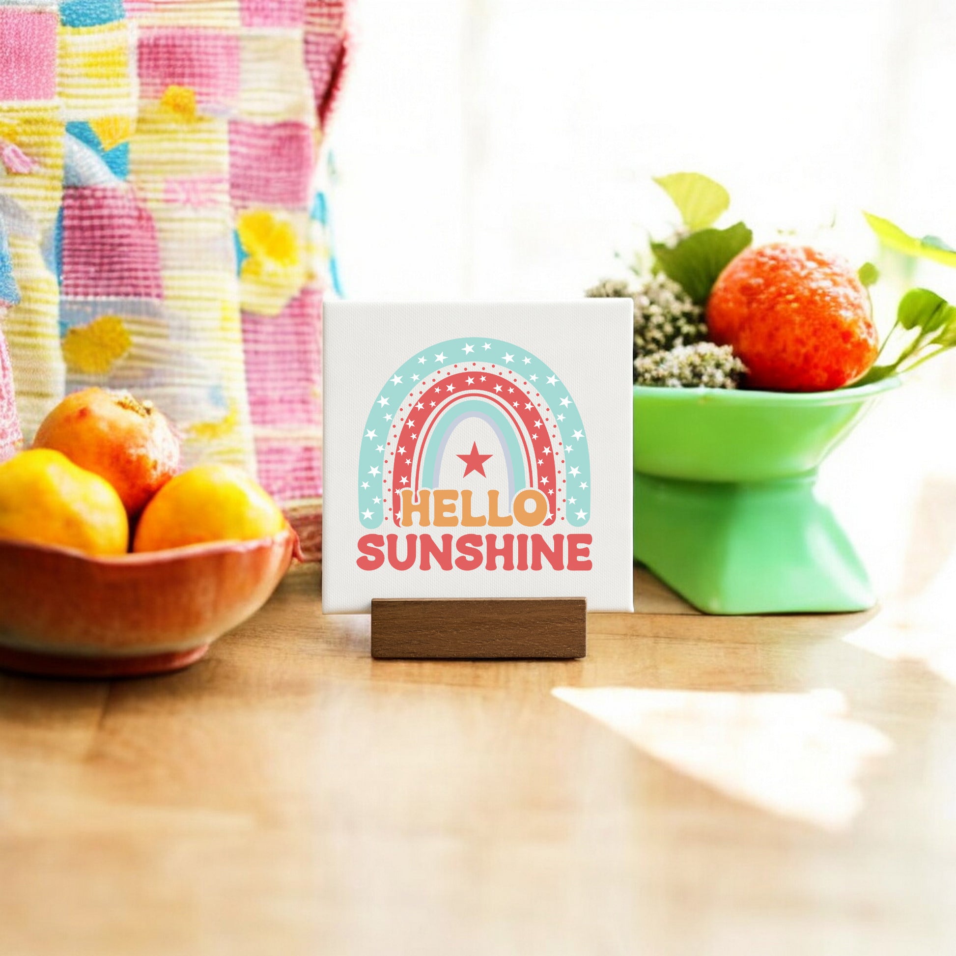 The Mirabilia Boutique Hello Sunshine Mini Canvas Sign with Stand adds a retro touch, featuring a rainbow design—perfect as a cheerful home accent on any sunlit table.