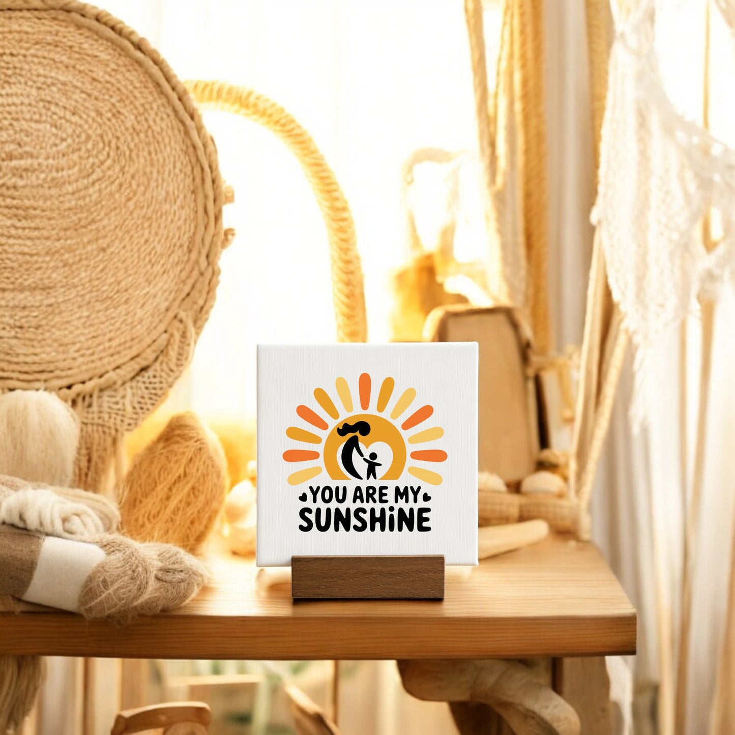 The "You Are My Sunshine Mini Sign – Mom & Child Canvas" by Mirabilia Boutique features a sun graphic on a wooden stand, creating a heartfelt Mother’s Day gift perfect for cozy displays with baskets, yarn, and sunlight.