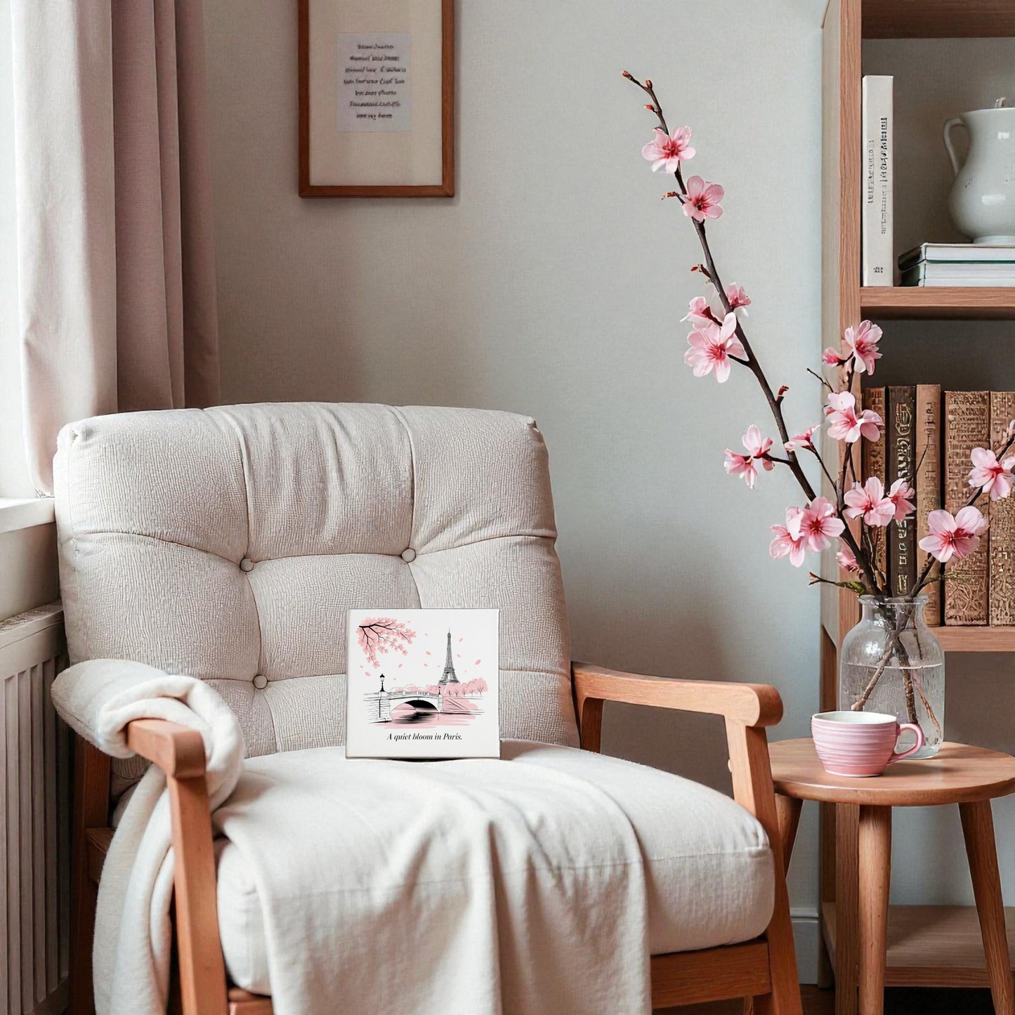 Create a cozy reading nook with a cushioned armchair, blanket, and Mirabilia Boutique’s Quiet Bloom in Paris Canvas – Cherry Blossom Spring Art. Add a table with pink flowers and cup for charming spring decor—bookshelves complete the scene.
