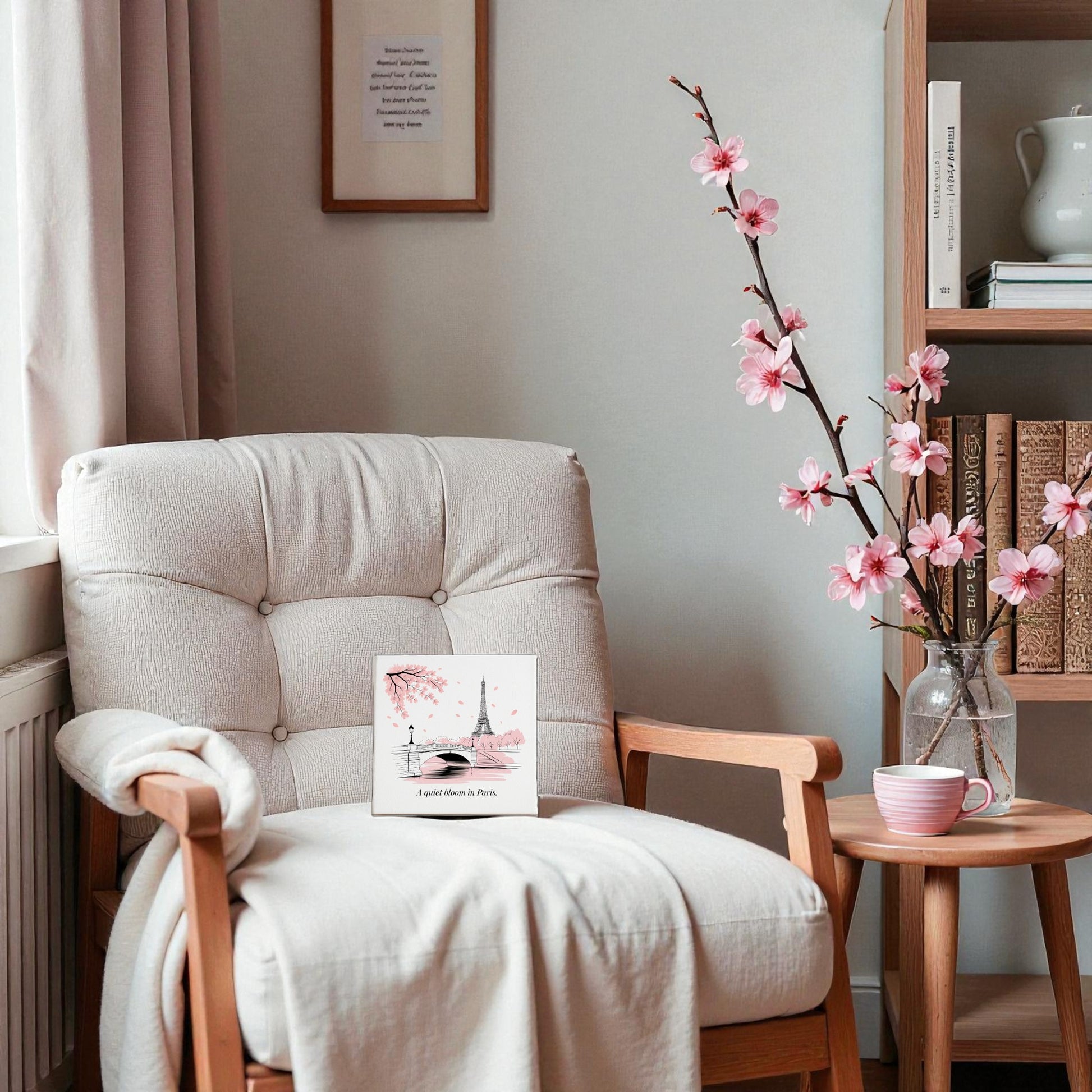 Create a cozy reading nook with a cushioned armchair, blanket, and Mirabilia Boutique’s Quiet Bloom in Paris Canvas – Cherry Blossom Spring Art. Add a table with pink flowers and cup for charming spring decor—bookshelves complete the scene.