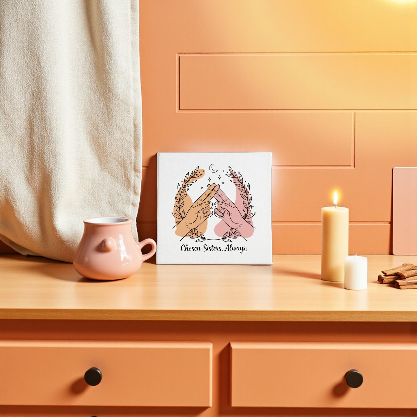 A peach-toned room features a wooden dresser with a pink teapot, candle, and the "Chosen Sisters Canvas | Friendship Gift for Best Friends" by Mirabilia Boutique—showing hands high-fiving with "Chosen Sisters. Always." Perfect for sisterhood.