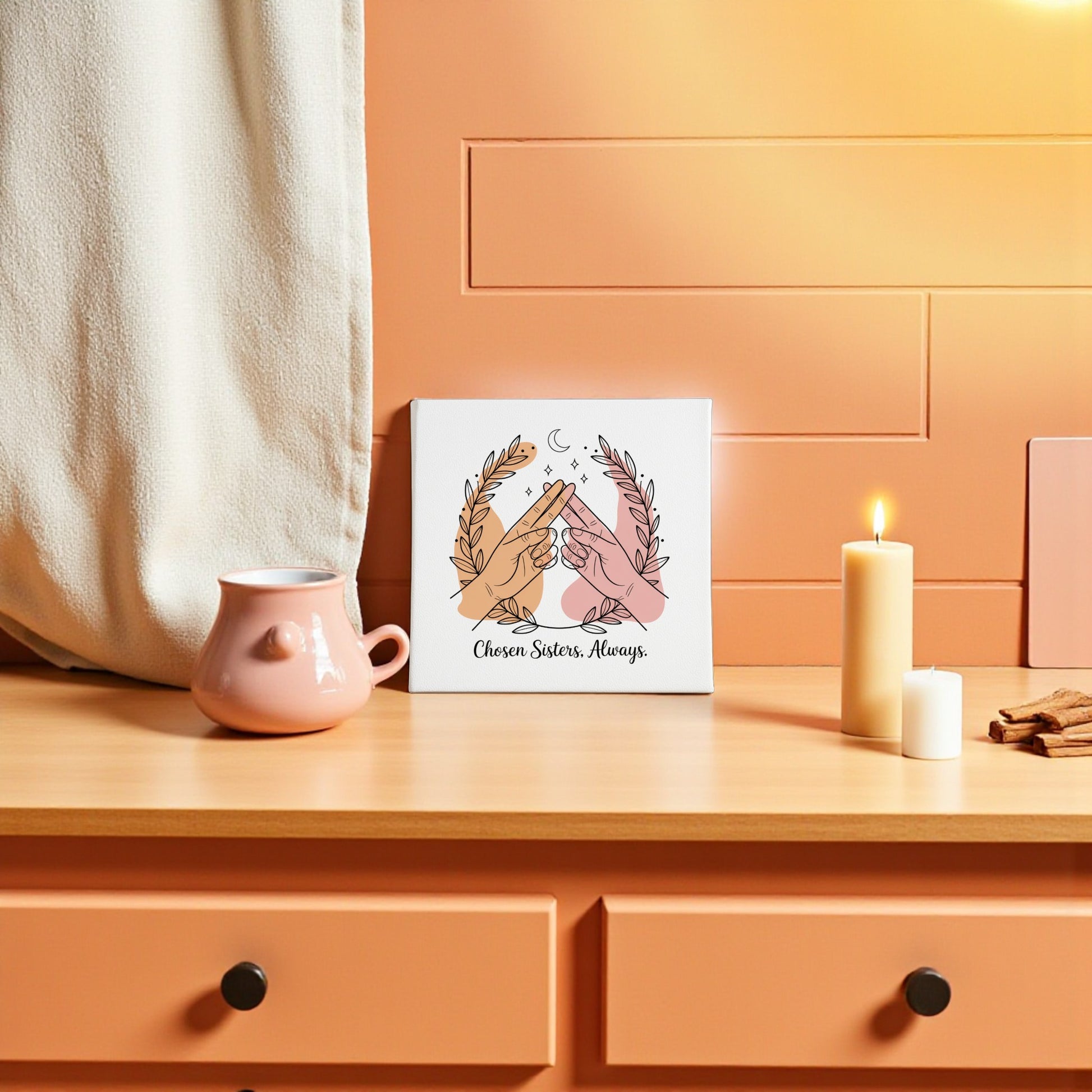 A peach-toned room features a wooden dresser with a pink teapot, candle, and the "Chosen Sisters Canvas | Friendship Gift for Best Friends" by Mirabilia Boutique—showing hands high-fiving with "Chosen Sisters. Always." Perfect for sisterhood.