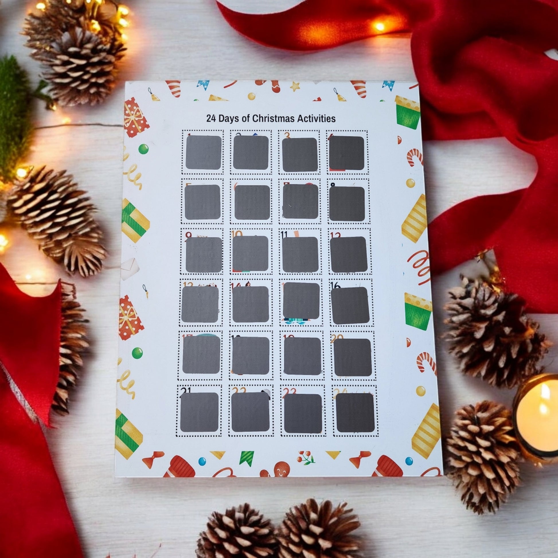 A "24 Days of Christmas Activities Scratch Off Calendar" from Mirabilia Boutique sits on a white wooden surface, surrounded by pine cones, red ribbons, and fairy lights. This holiday décor item features festive motifs like candy canes and gifts, offering plenty of holiday cheer.