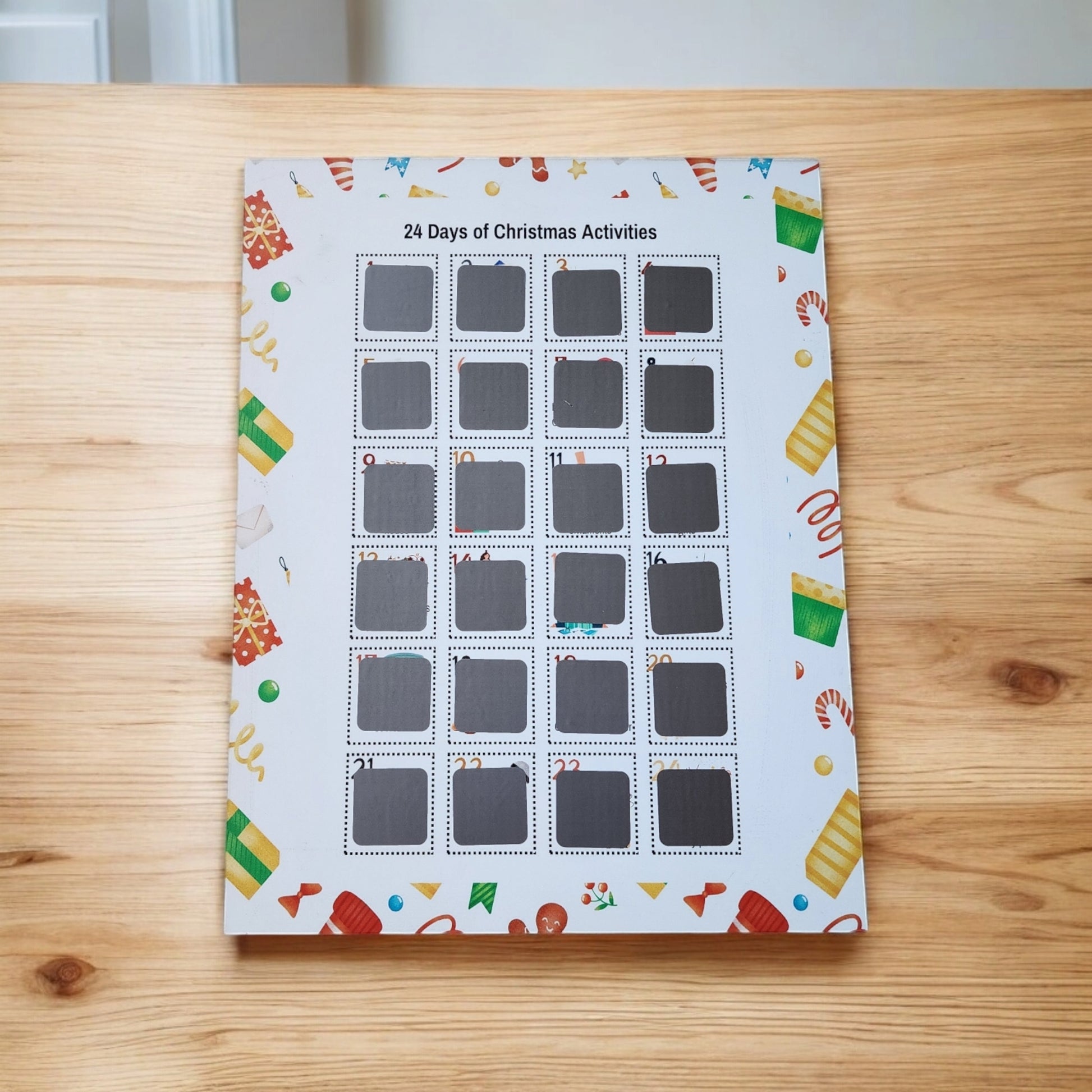 The "24 Days of Christmas Activities Scratch Off Calendar" by Mirabilia Boutique sits on a wooden table, featuring 24 windows perfect for festive fun. Each window is numbered for December days and adorned with candy canes, gifts, and holiday décor.