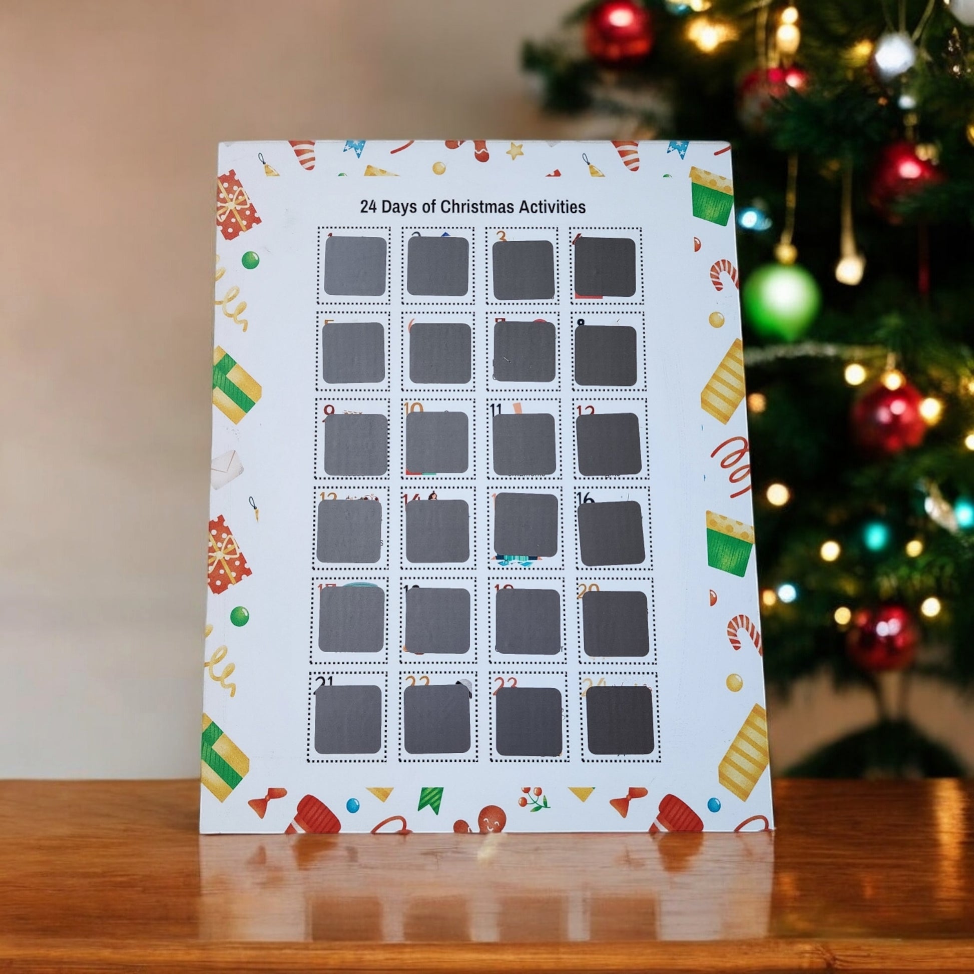 A "24 Days of Christmas Activities Scratch Off Calendar" from Mirabilia Boutique sits on a wooden table, promising festive fun. Adorned with cheerful patterns, this calendar features 24 slots for unique holiday activities. In the background, a Christmas tree glimmers with colorful ornaments.