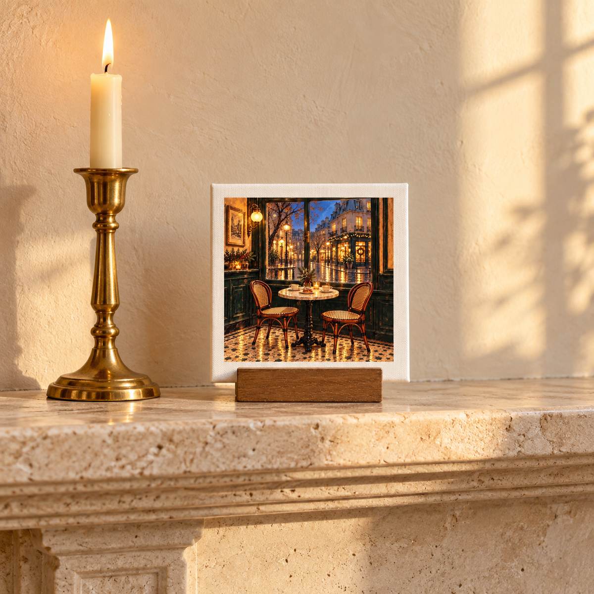 A Table for Christmas Eve Mini Sign | Paris Toujours, a square canvas panel on a wooden stand, depicts a cozy Parisian cafe table set for Christmas Eve, displayed on a mantel next to a lit brass candlestick.