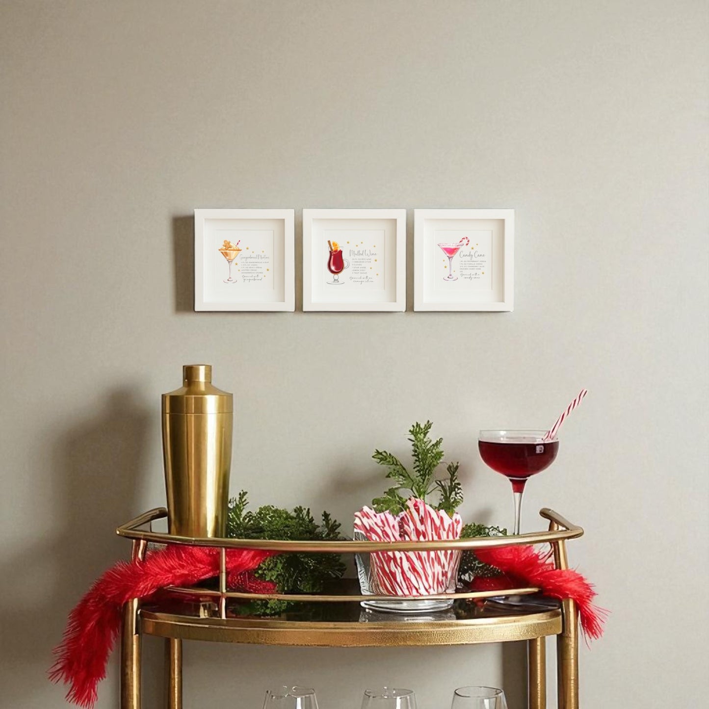 A gold bar cart with a cocktail, candy canes, and festive greenery sits below the Mirabilia Boutique Classic Christmas Cocktails 5x5 Shadowbox Trio. Three framed holiday bar art pieces hang above, accented by a red feathery garland for extra cheer.