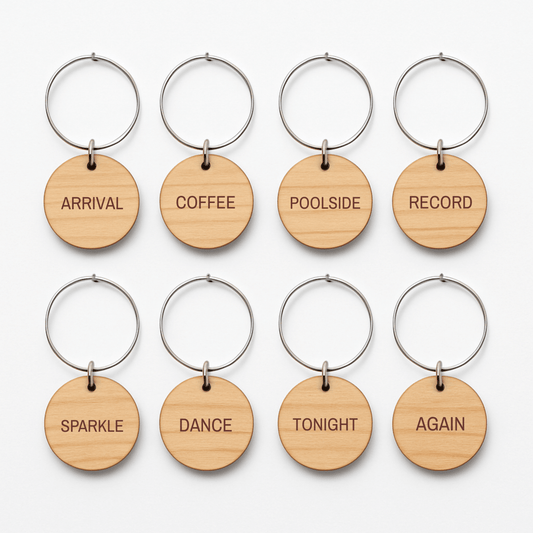 Eight circular wooden Chrome & Starlight Wood Wine Charms on silver metal rings, each engraved with a unique word: “Arrival,” “Coffee,” “Poolside,” “Record,” “Sparkle,” “Dance,” “Tonight,” and “Again.”.