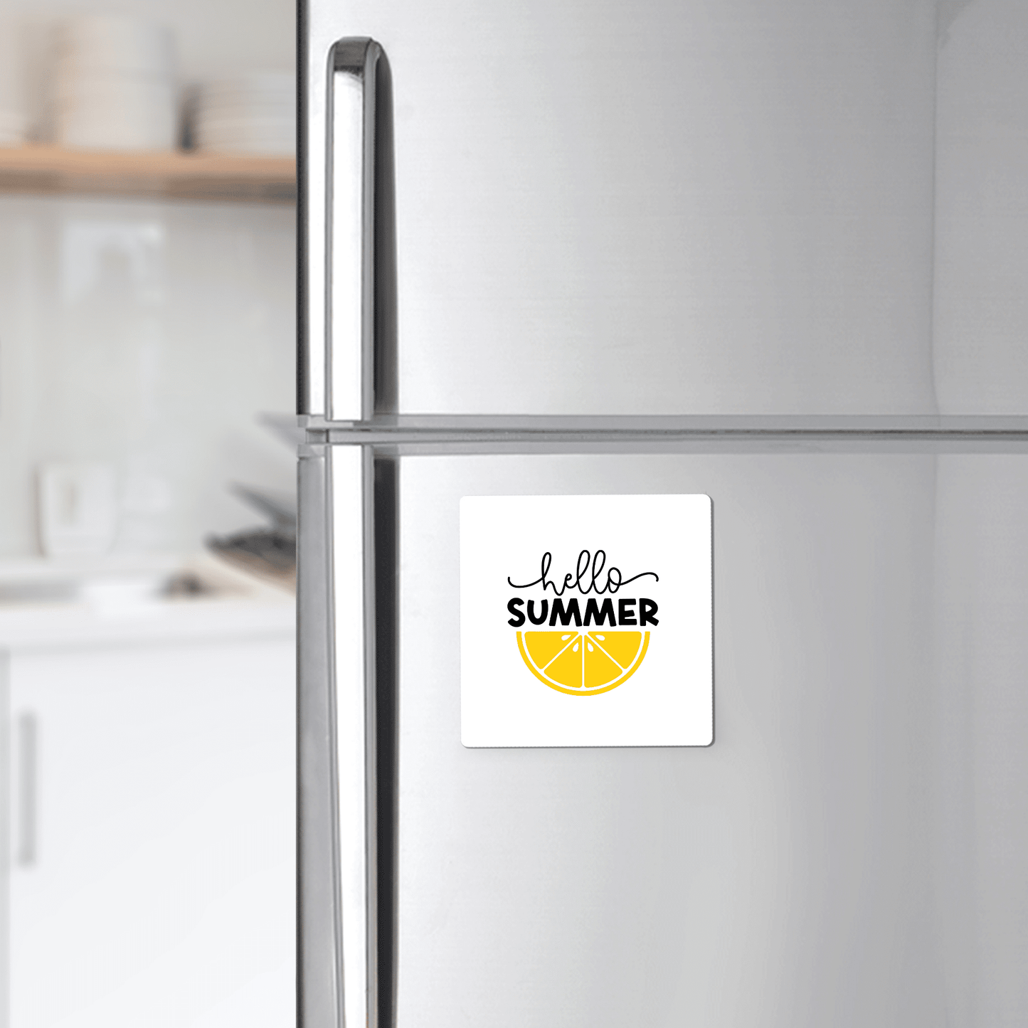 A silver fridge displays the Mirabilia Boutique Hello Summer Lemon Magnet – Bold Citrus Fridge Art, a square magnet with "hello SUMMER" above a yellow lemon slice. Blurred shelves and dishes accent the summer kitchen scene.
