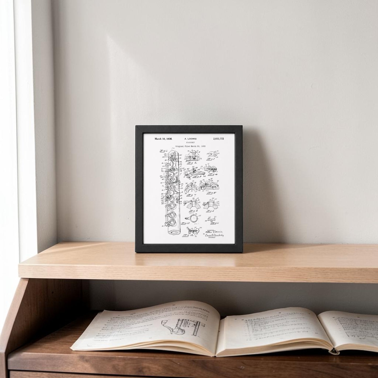The Clarinet Patent Print on Metal Wall Art by Mirabilia Boutique is displayed on a wooden shelf against a light gray wall with an open book below—ideal music room decor, illuminated by natural light from the left.