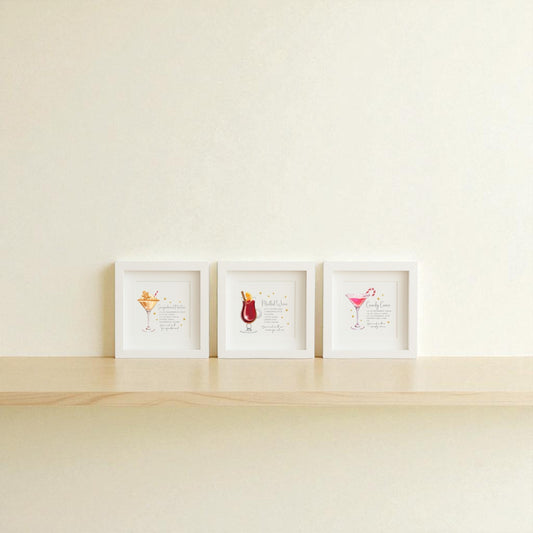 The Classic Christmas Cocktails 5x5 Shadowbox Trio by Mirabilia Boutique features festive holiday bar art, displayed side by side on a light wooden shelf against an off-white wall.