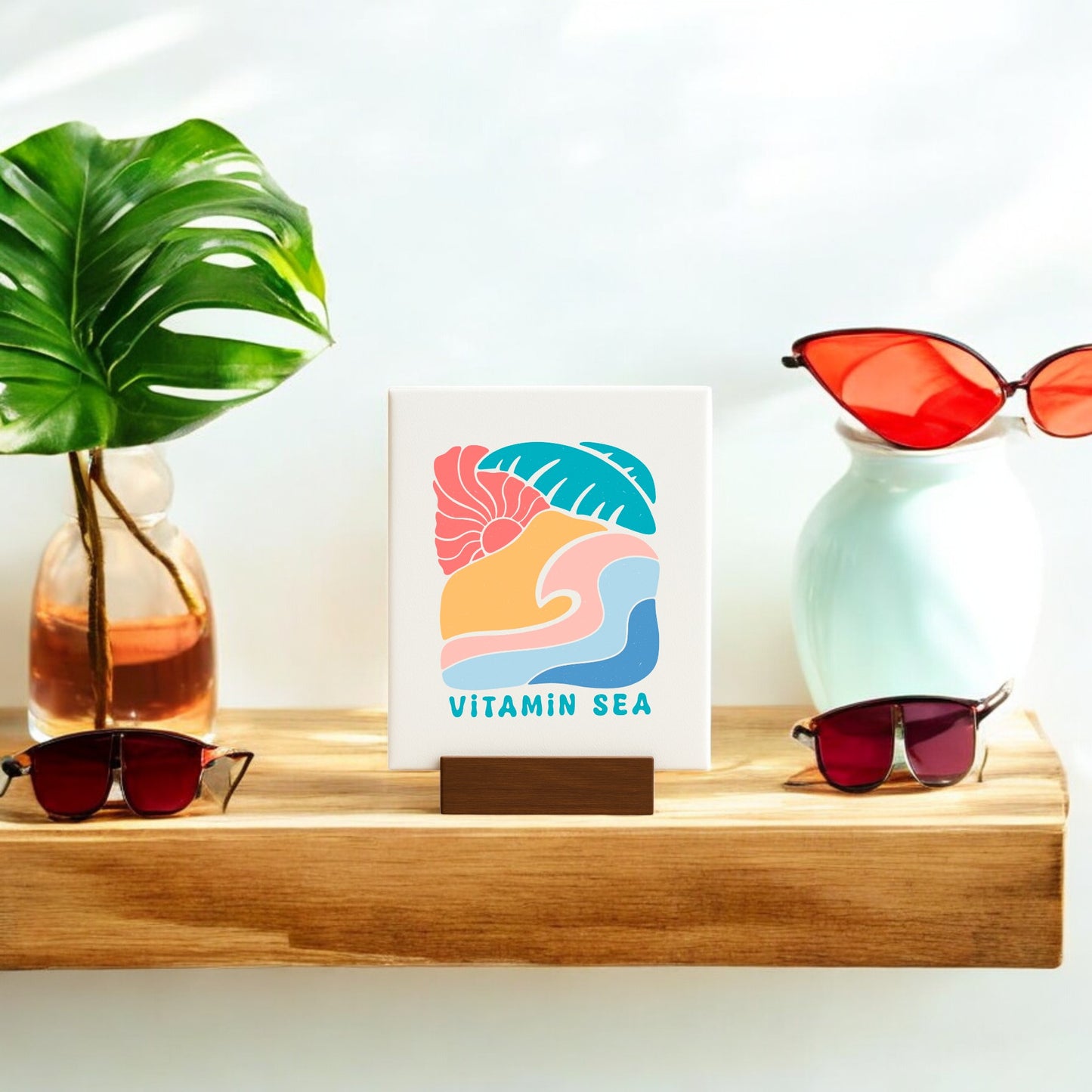A wooden shelf features a tropical leaf in a vase, two pairs of red sunglasses, and the Mirabilia Boutique Vitamin Sea Mini Canvas Sign – 4x6 Coastal Decor, perfect for bringing coastal style to any room.