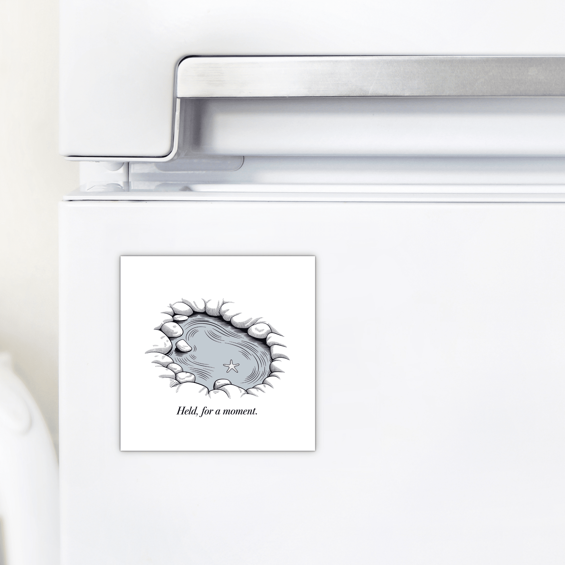 The "Held, for a Moment – Coastal Reflection Magnet" by Mirabilia Boutique adorns your fridge with a serene pond, rocks, starfish, and grass. The calming design features the phrase “Held for a moment”—a soothing ocean-inspired decor accent.