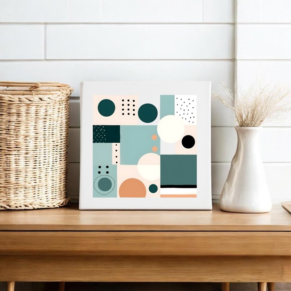 The Coastal Geometry Mid Century Modern Canvas by Mirabilia Boutique, featuring teal, peach, beige, and black abstract shapes, is displayed on a wooden table beside a woven basket and white vase with dried grass against a shiplap wall.