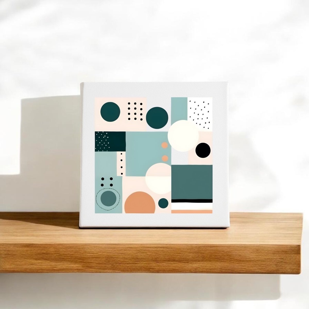 The Coastal Geometry Mid Century Modern Canvas by Mirabilia Boutique features abstract geometric shapes in teal, peach, black, and white. This small white canvas rests on a light wooden shelf against a plain white background.