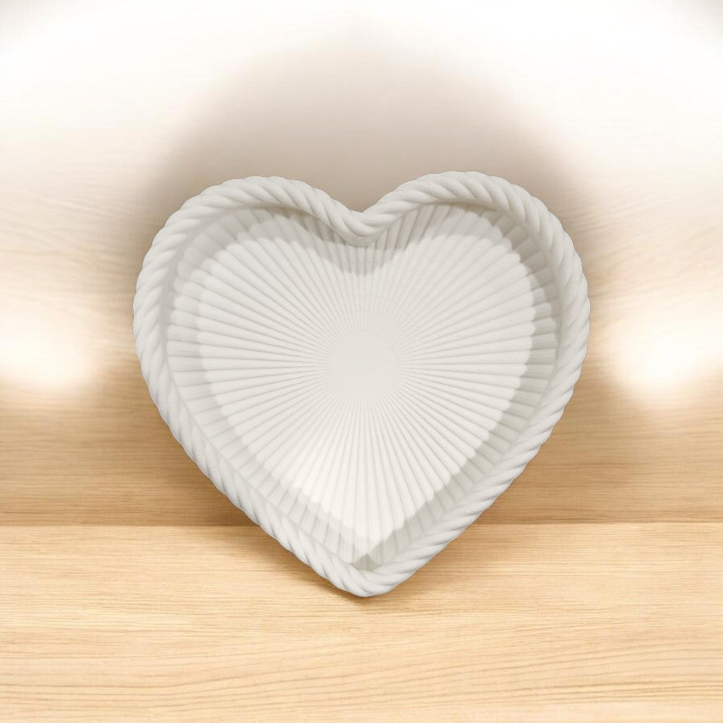The Mirabilia Boutique Coastal Heart Tray in Matte White, with its textured ridged pattern and rope-like border, brings beach-inspired charm to any space as it rests on a light wooden surface against a softly lit backdrop.