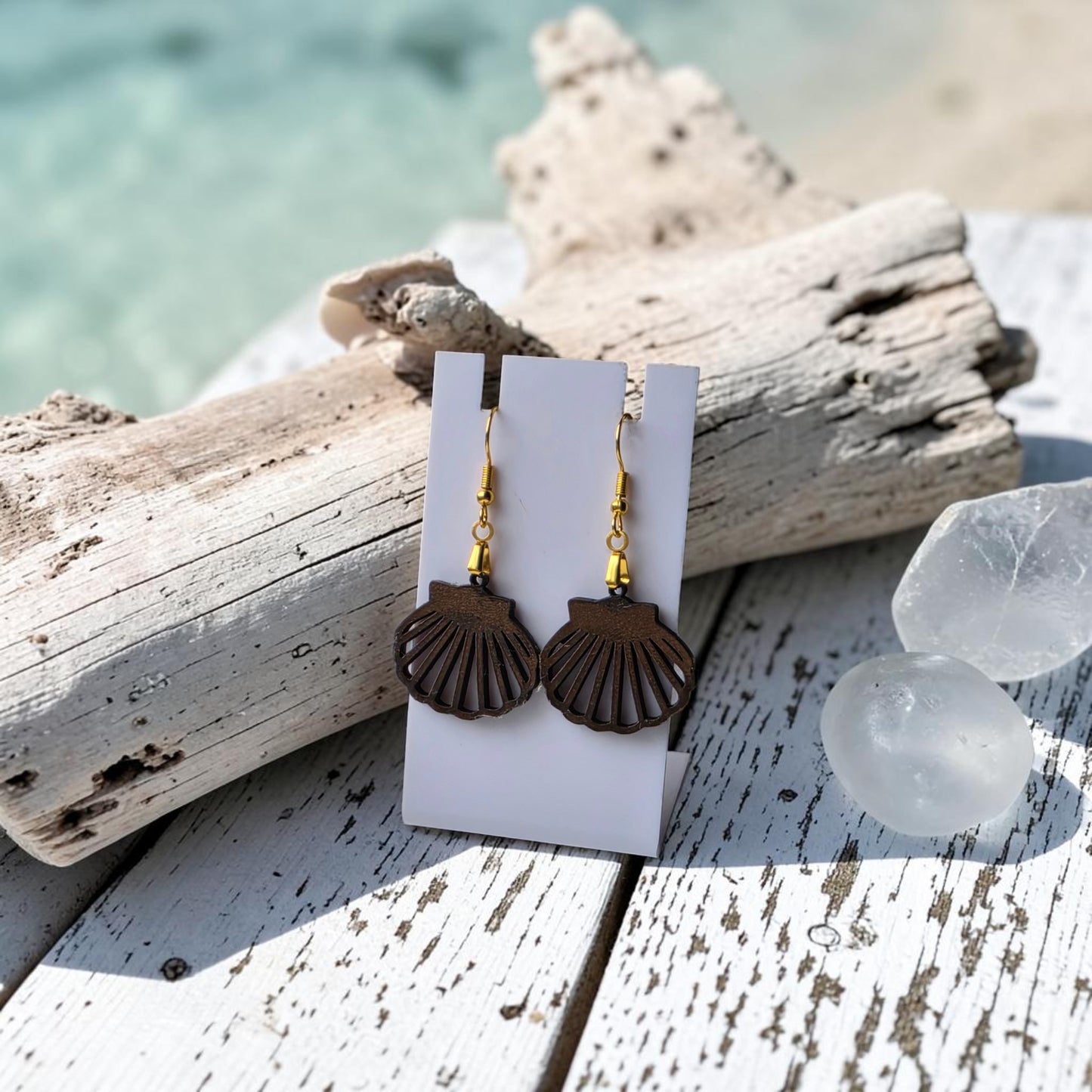 Scallop Shell Earrings | Lasercut Walnut Wood by Mirabilia Boutique—gold-hook earrings displayed on a white card over rustic wood, driftwood, and crystals, with a blurred beach view. Perfect coastal jewelry for ocean lovers.